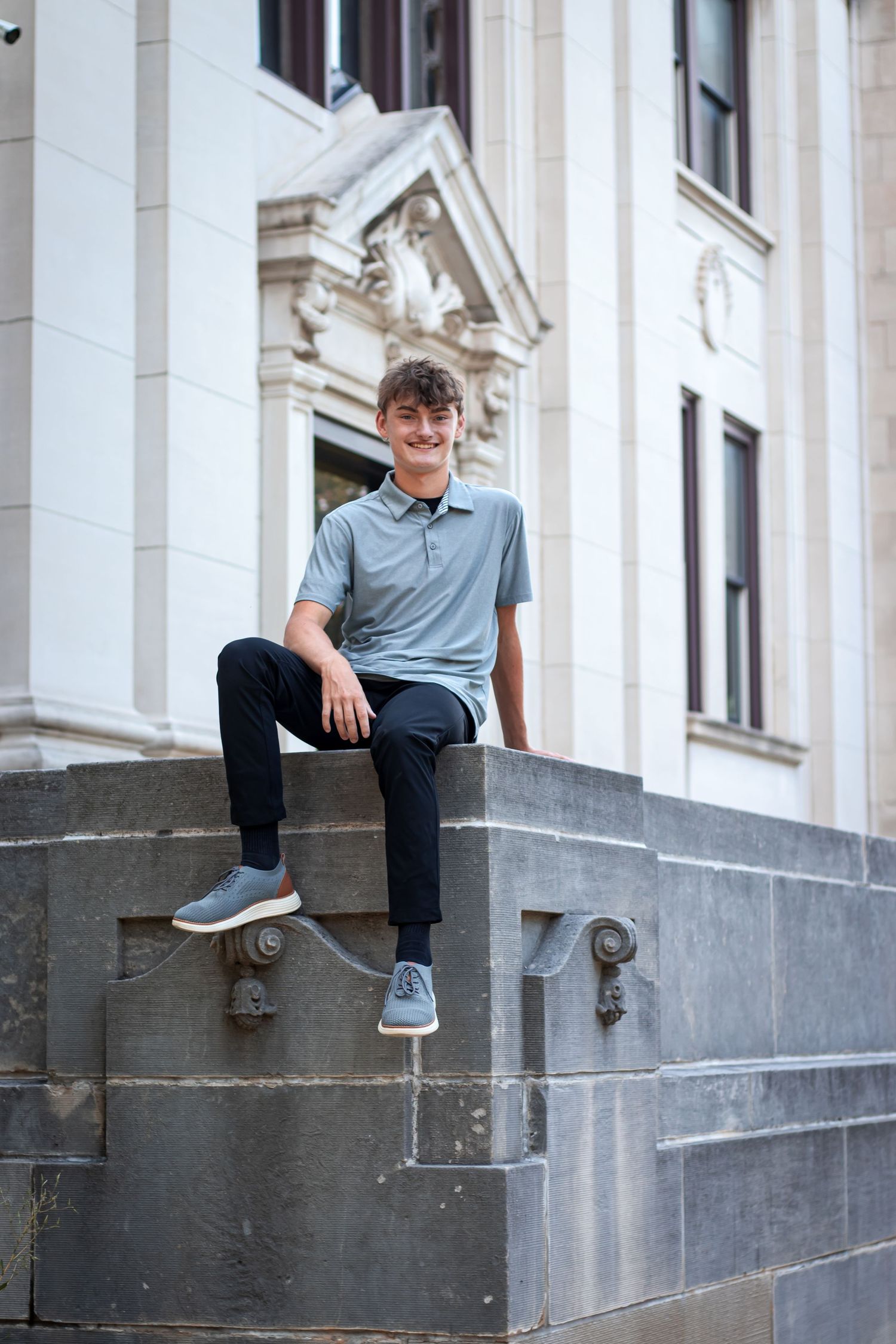 Smiling teenage boy sitting on stone steps outside a classic building.
