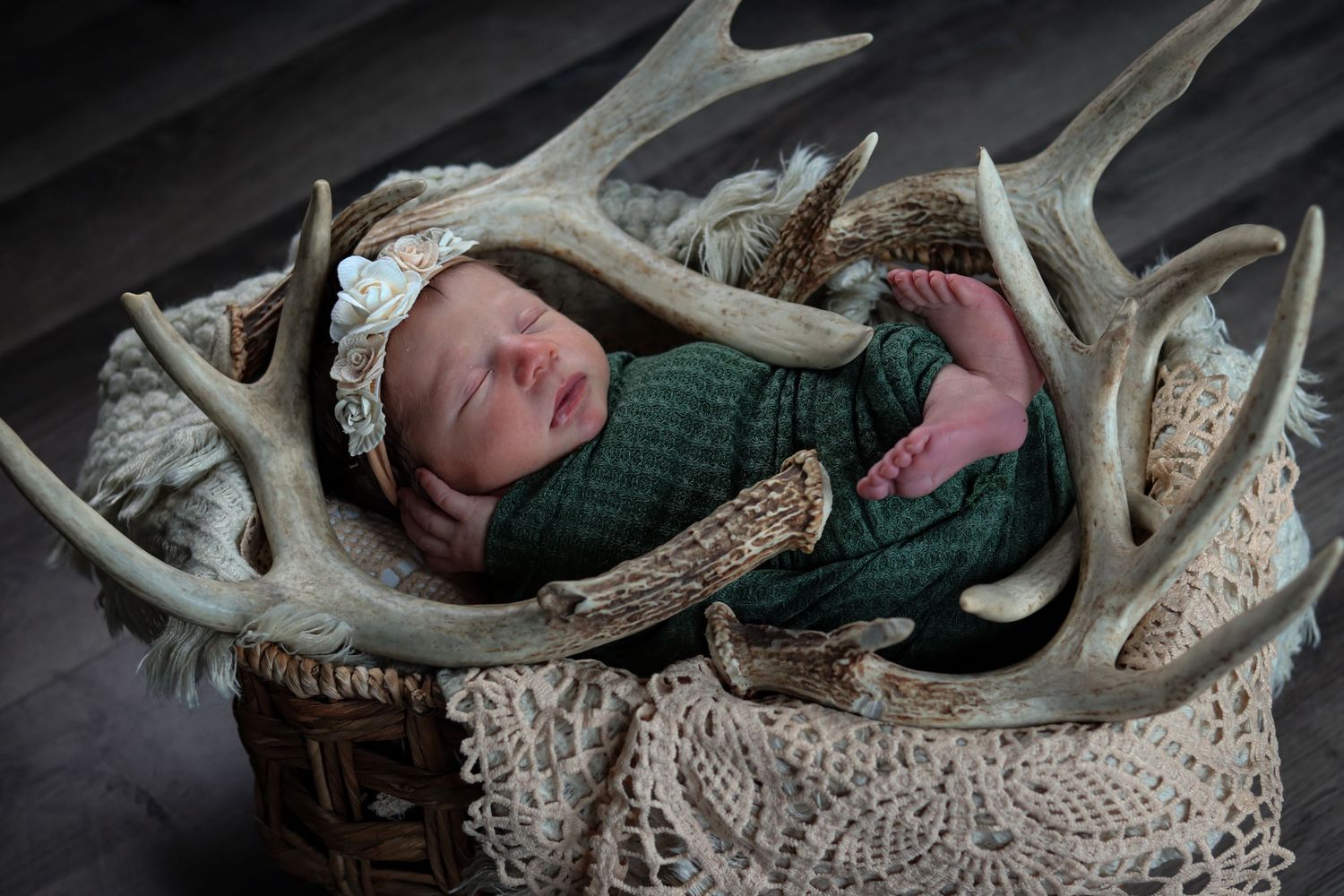 Sleeping newborn baby wrapped in green swaddle nestled among deer antlers.