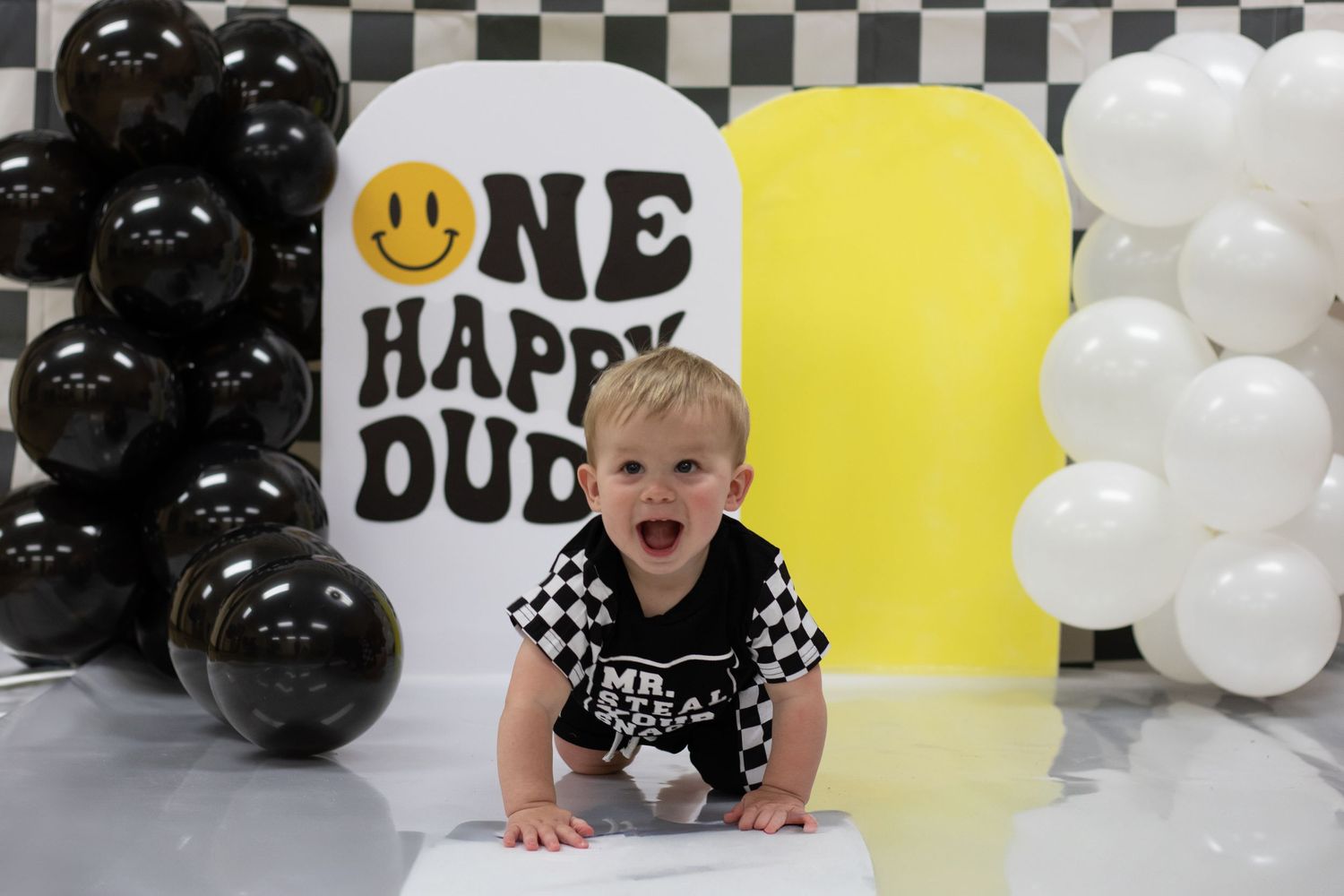 Baby boy crawling at One Happy Dude first birthday party with black and white checkered balloons.