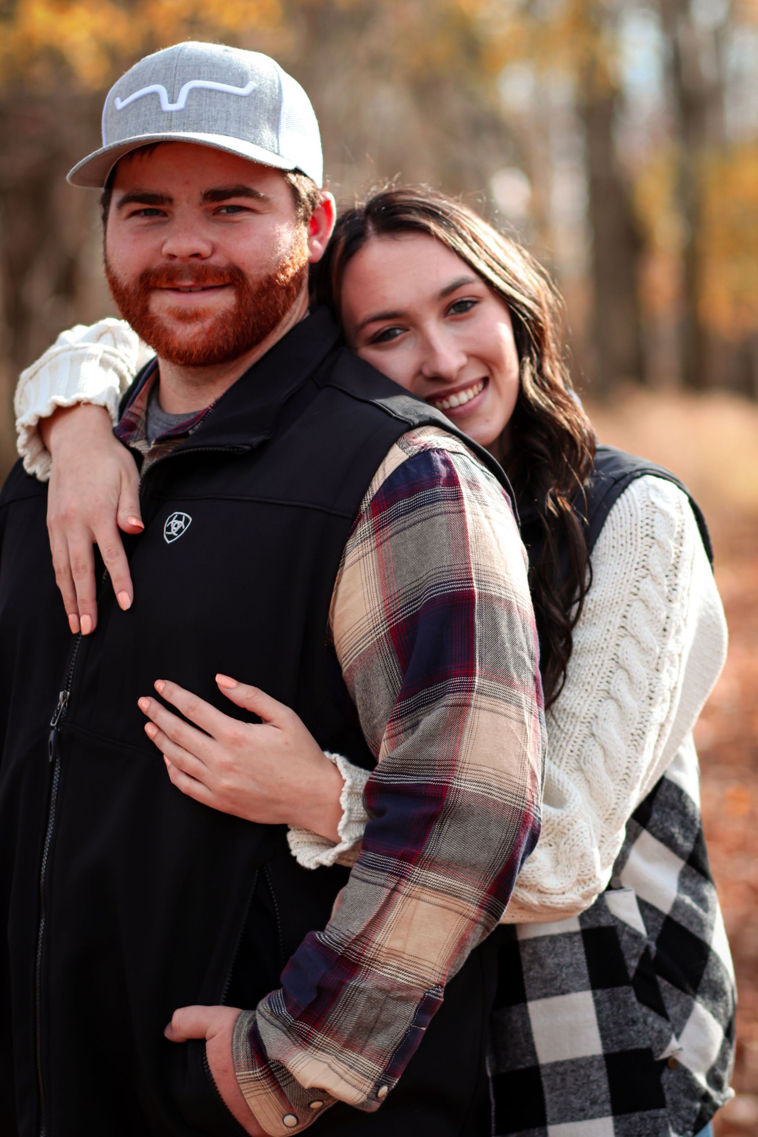 Smiling couple embracing in autumn forest with colorful foliage.