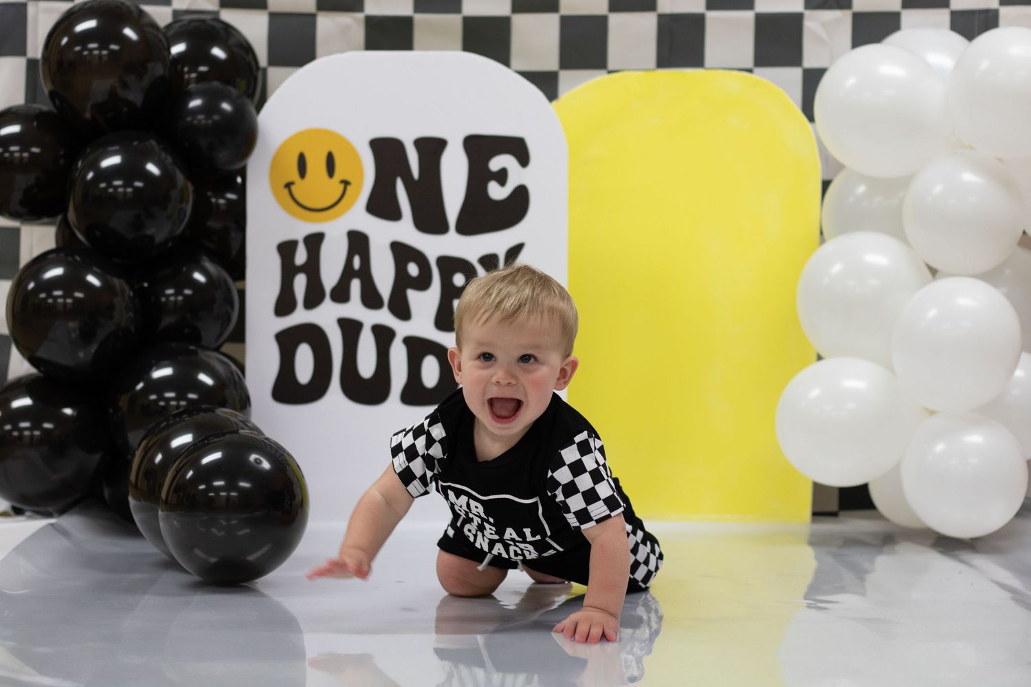 Baby boy celebrates first birthday with One Happy Dude checkered racing theme with black and white balloons.