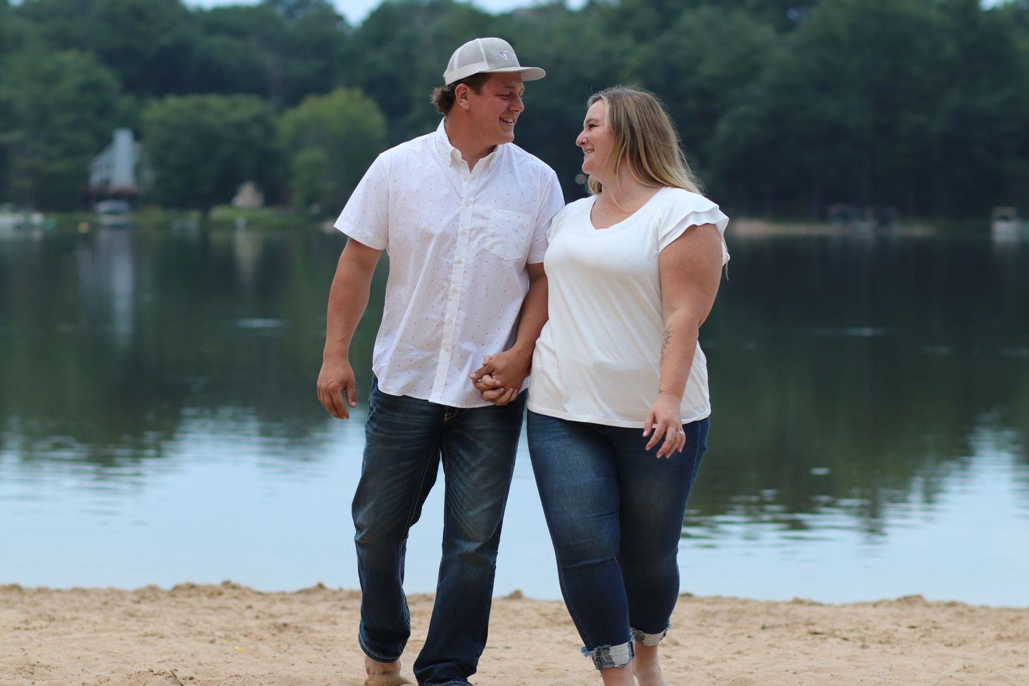Couple holding hands and walking on a sandy beach by a lake.