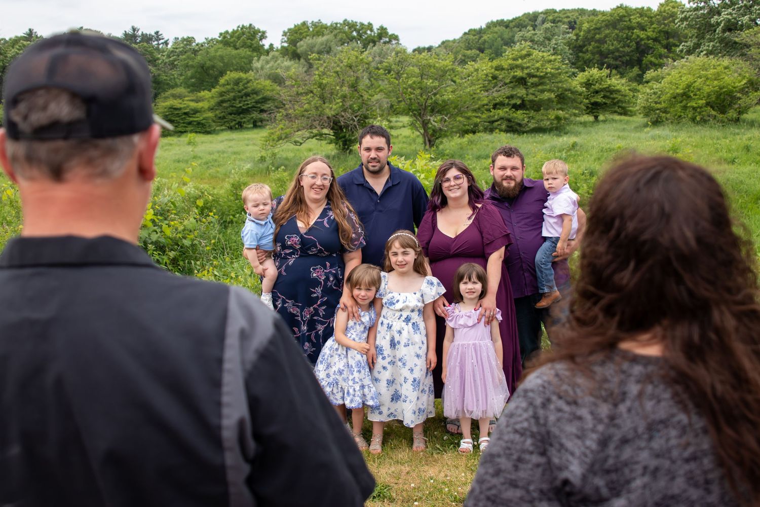 A large family group poses for an outdoor portrait in a lush green meadow during a professional photo session.