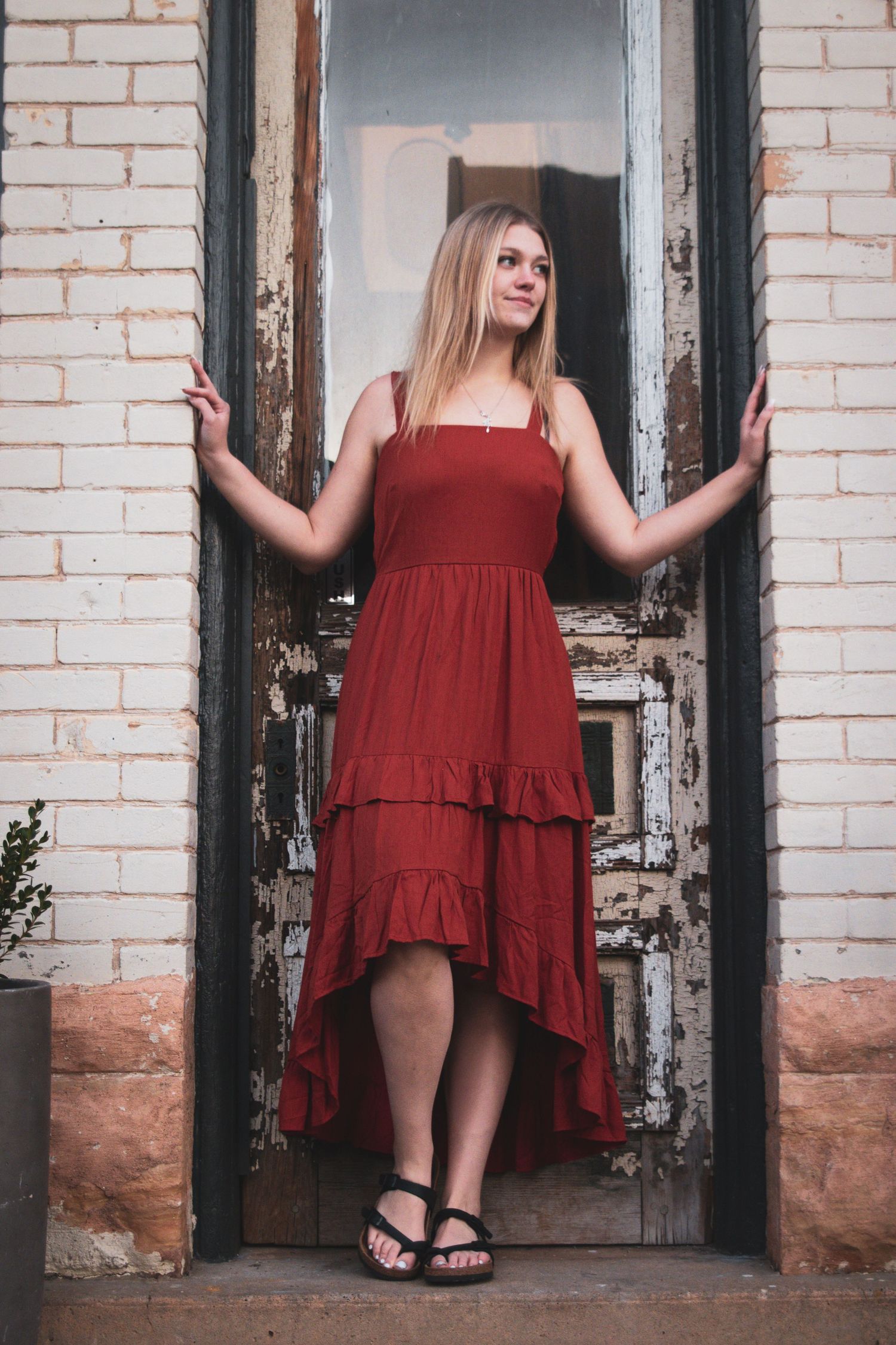 Young blonde woman in red ruffled dress posing in rustic doorway of brick building.