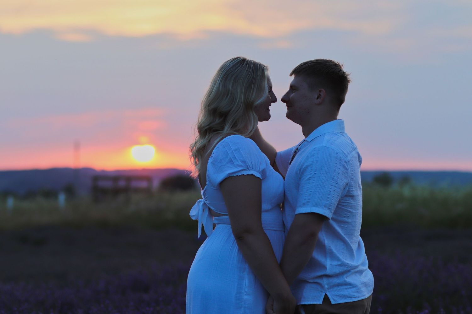 Pregnant couple sharing a romantic moment at sunset in a lavender field.
