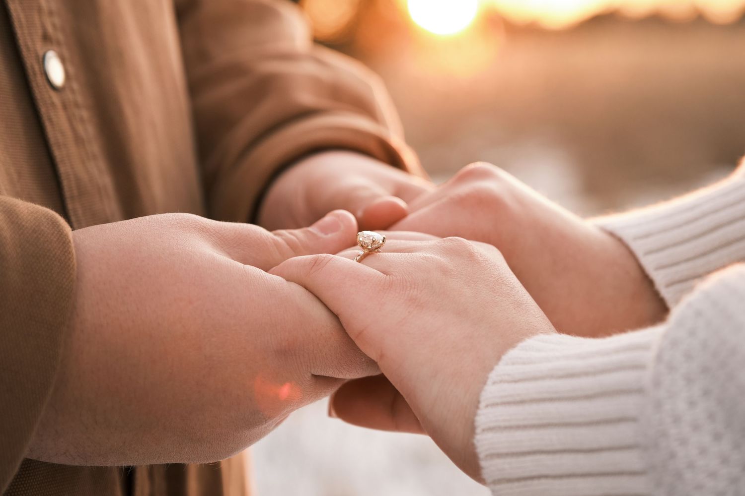 Close-up of couple holding hands at sunset, woman wearing a diamond engagement ring.