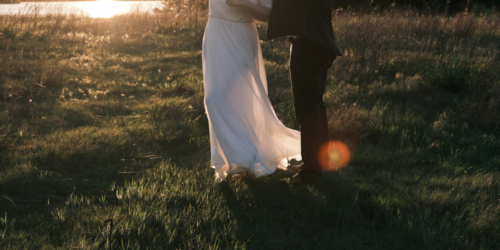 Bride and groom embracing in a sunlit field at golden hour, wedding dress flowing gracefully.