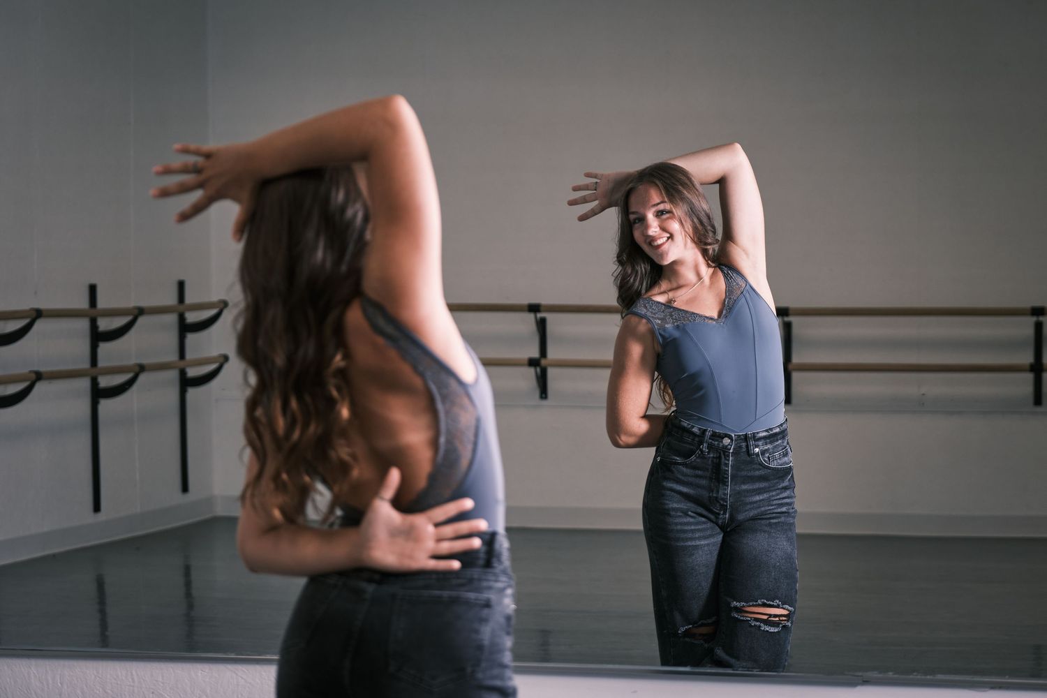 Young woman dancing and smiling at her reflection in a ballet studio mirror.