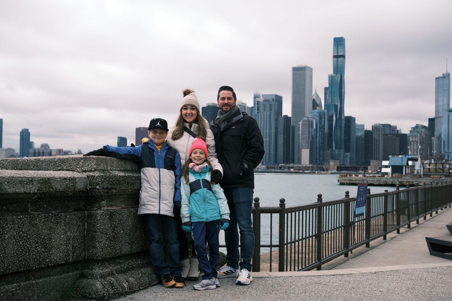 Family of four smiling together on a waterfront promenade with Chicago skyline in the background.