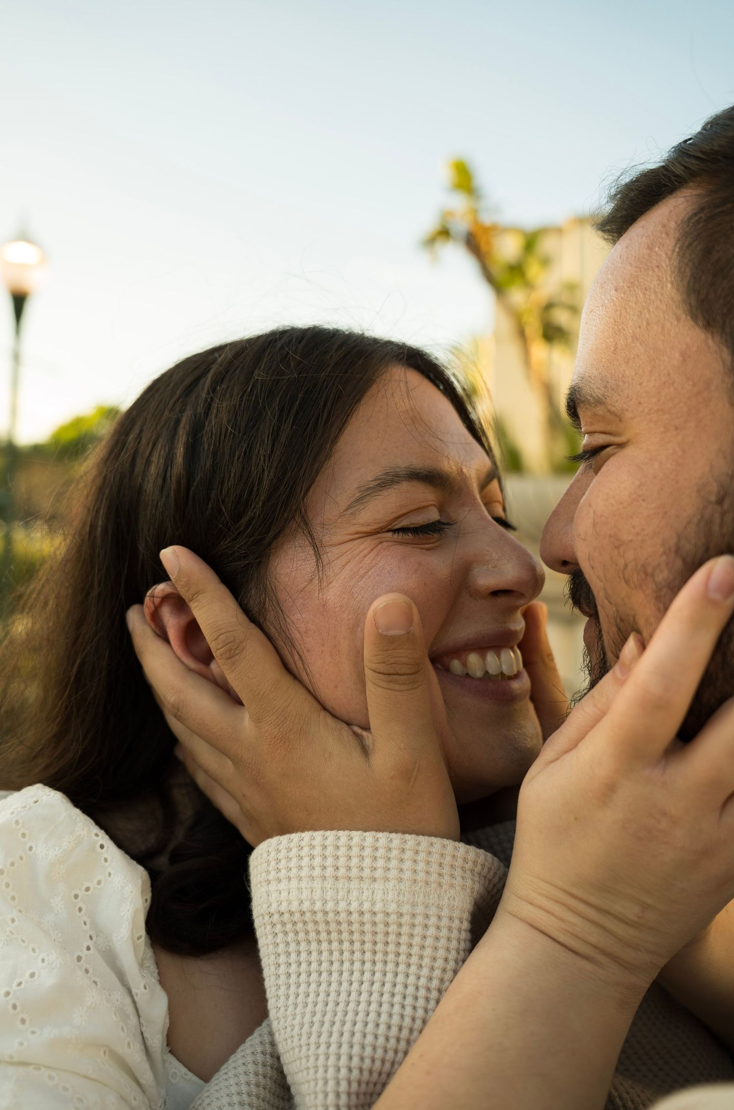 A couple holding each other's faces with their noses scrunched and smiling