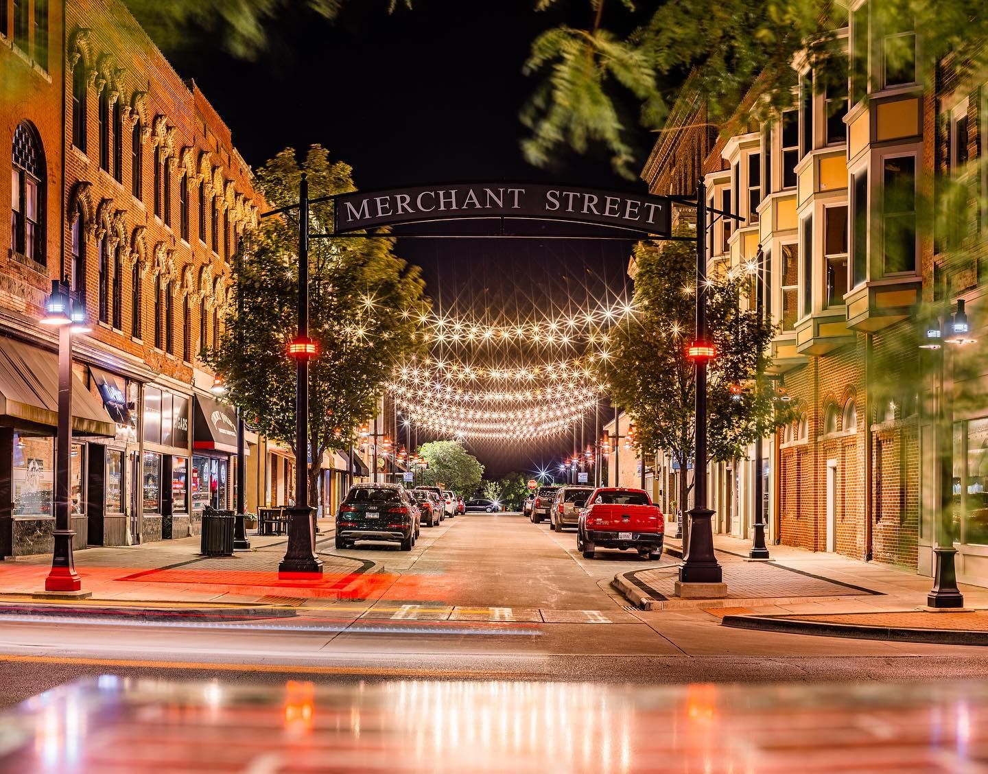 Merchant Street at night illuminated by string lights and red street lamps reflecting on wet pavement.