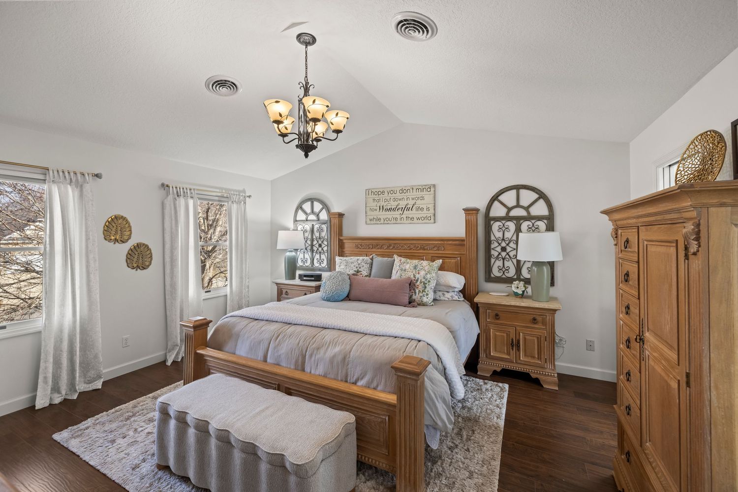 Elegant master bedroom with wooden furniture, chandelier, arched windows, and dark hardwood floors in a warm, inviting space.
