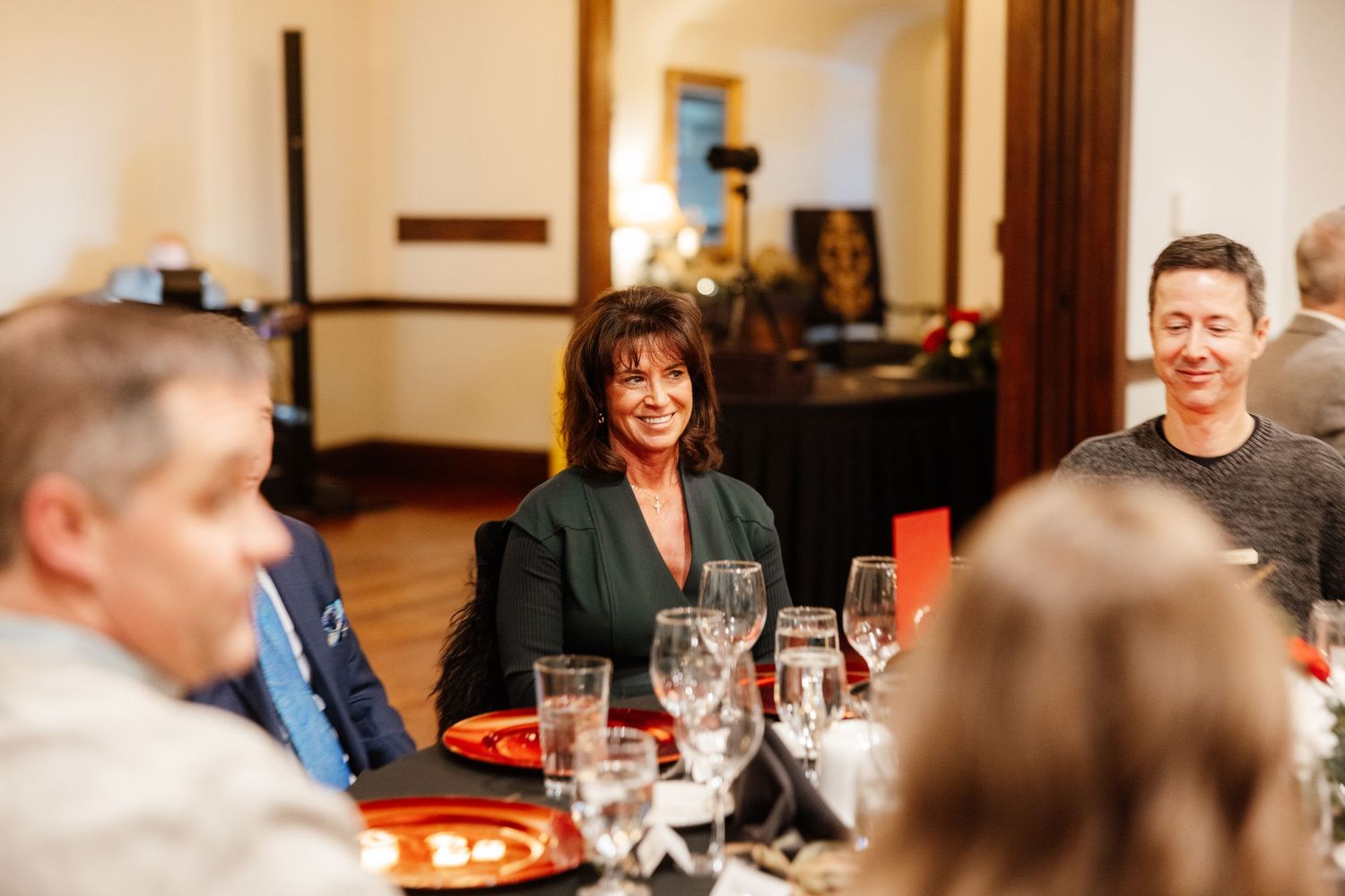 Woman in green blazer smiling at elegant dinner table during formal event gathering.