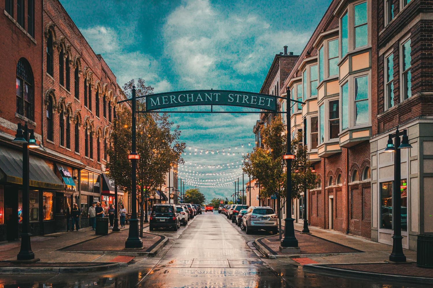 Merchant Street lined with historic brick buildings, string lights, and wet pavement under a cloudy sky.