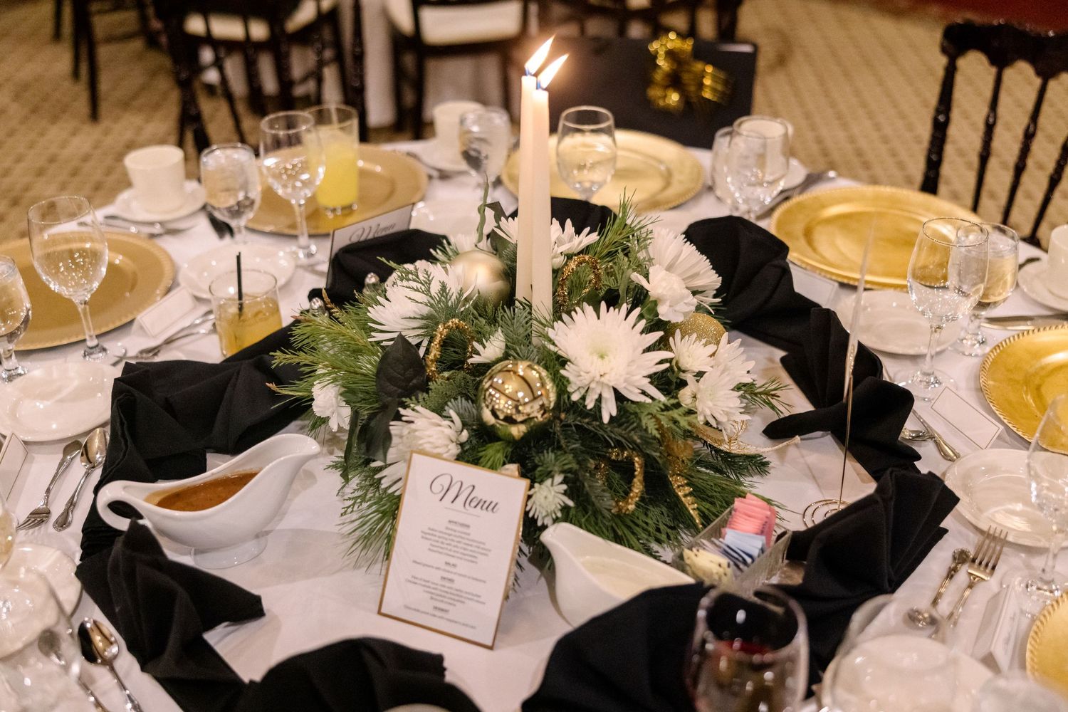 Elegant black and white wedding reception table setting with gold chargers, white flowers, and a lit candle centerpiece.