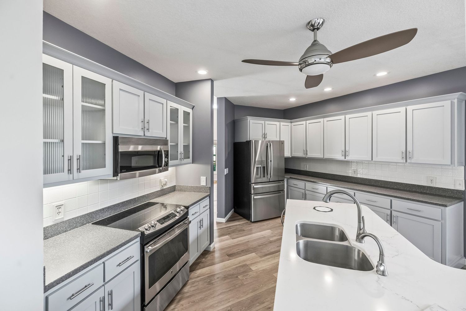 Modern kitchen with gray cabinets, stainless steel appliances, quartz countertops, and ceiling fan.
