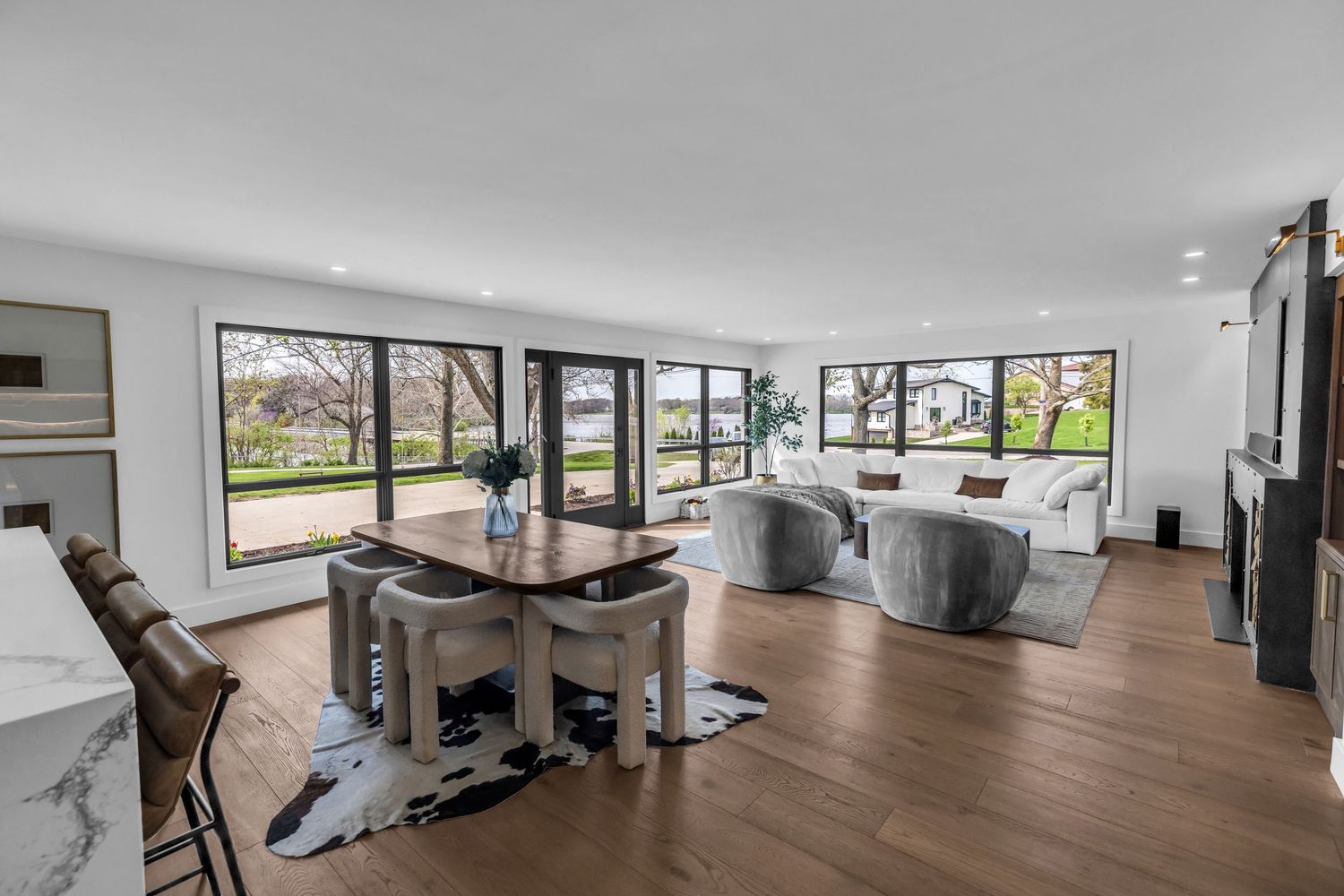 Open-concept living and dining area with hardwood floors, large windows, and modern neutral furnishings.