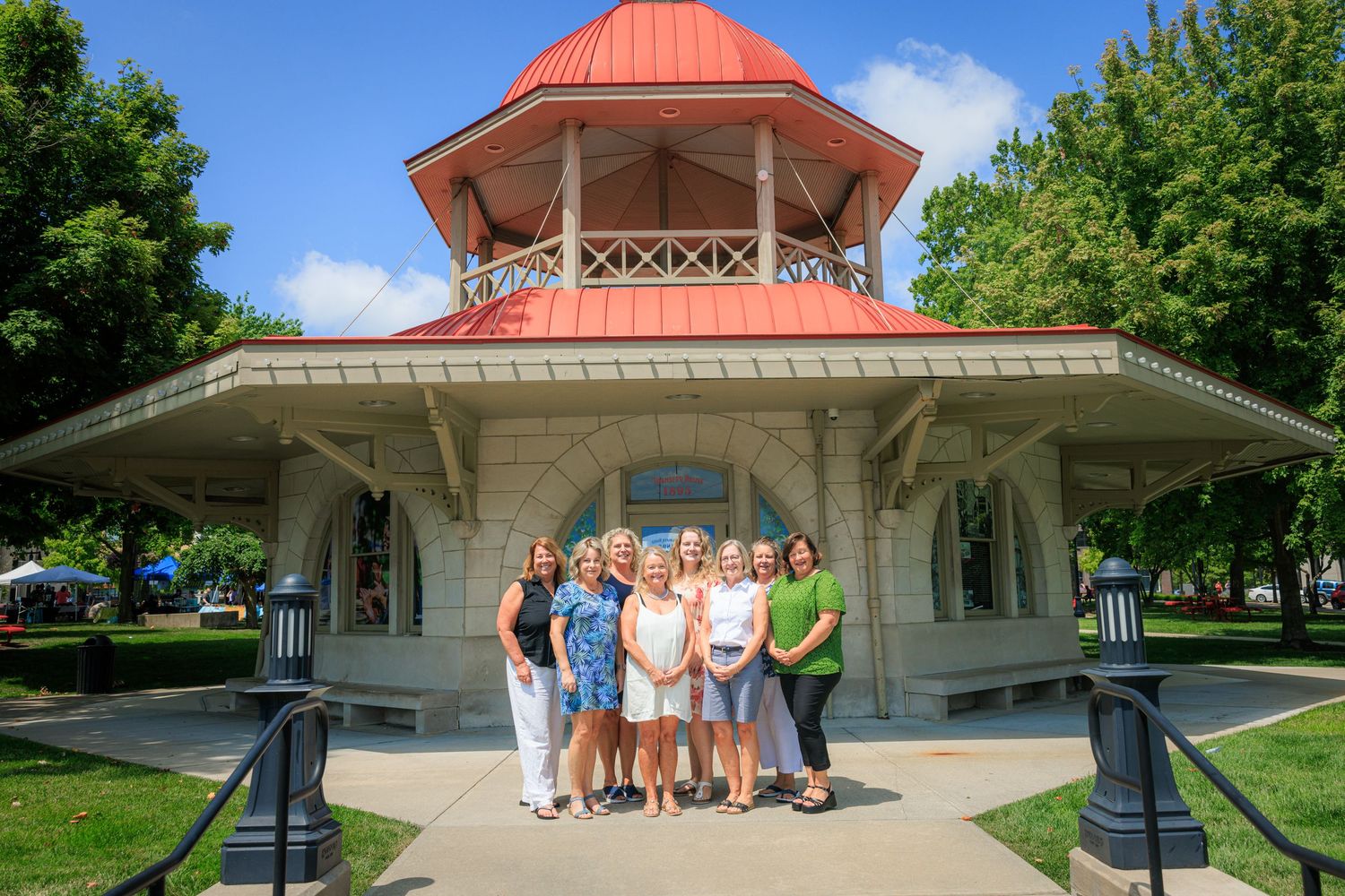 Group of women posing in front of a historic gazebo with a red roof on a sunny summer day.