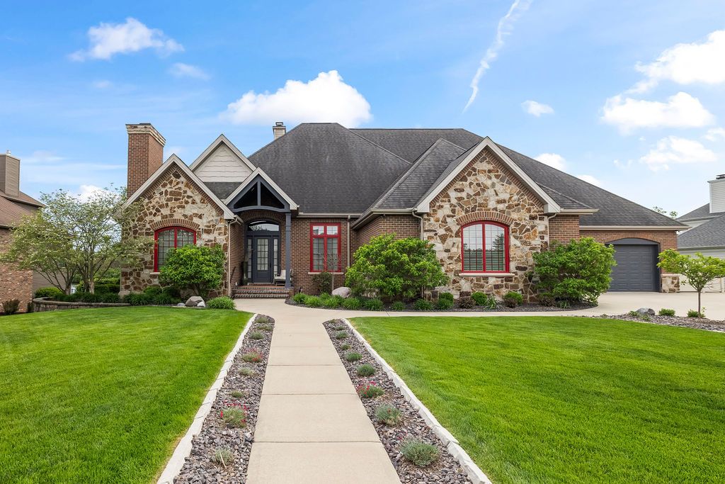 Elegant stone and brick ranch home with lush green lawn, manicured landscaping, and charming arched entryway.