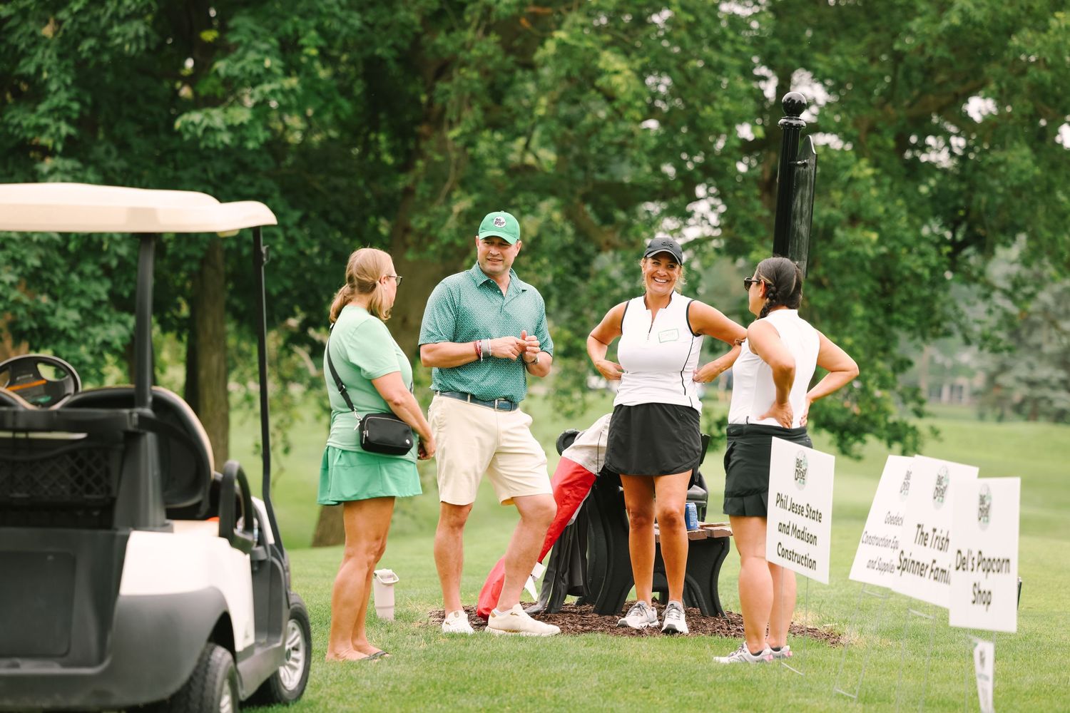 Golfers gather near a golf cart on a lush green course during a classic golf tournament event.