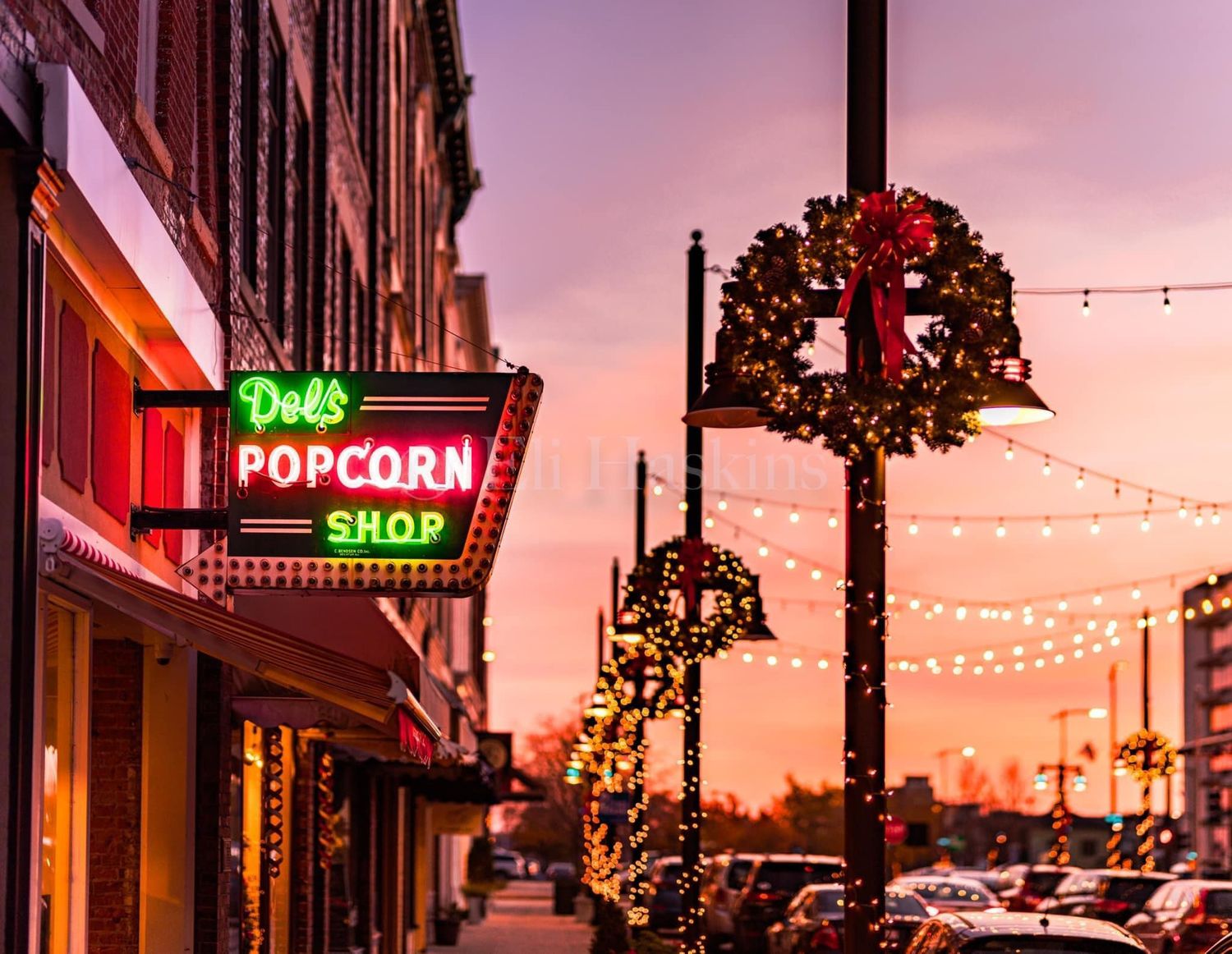 Del's Popcorn Shop neon sign glowing at sunset with Christmas wreaths and string lights decorating the street.
