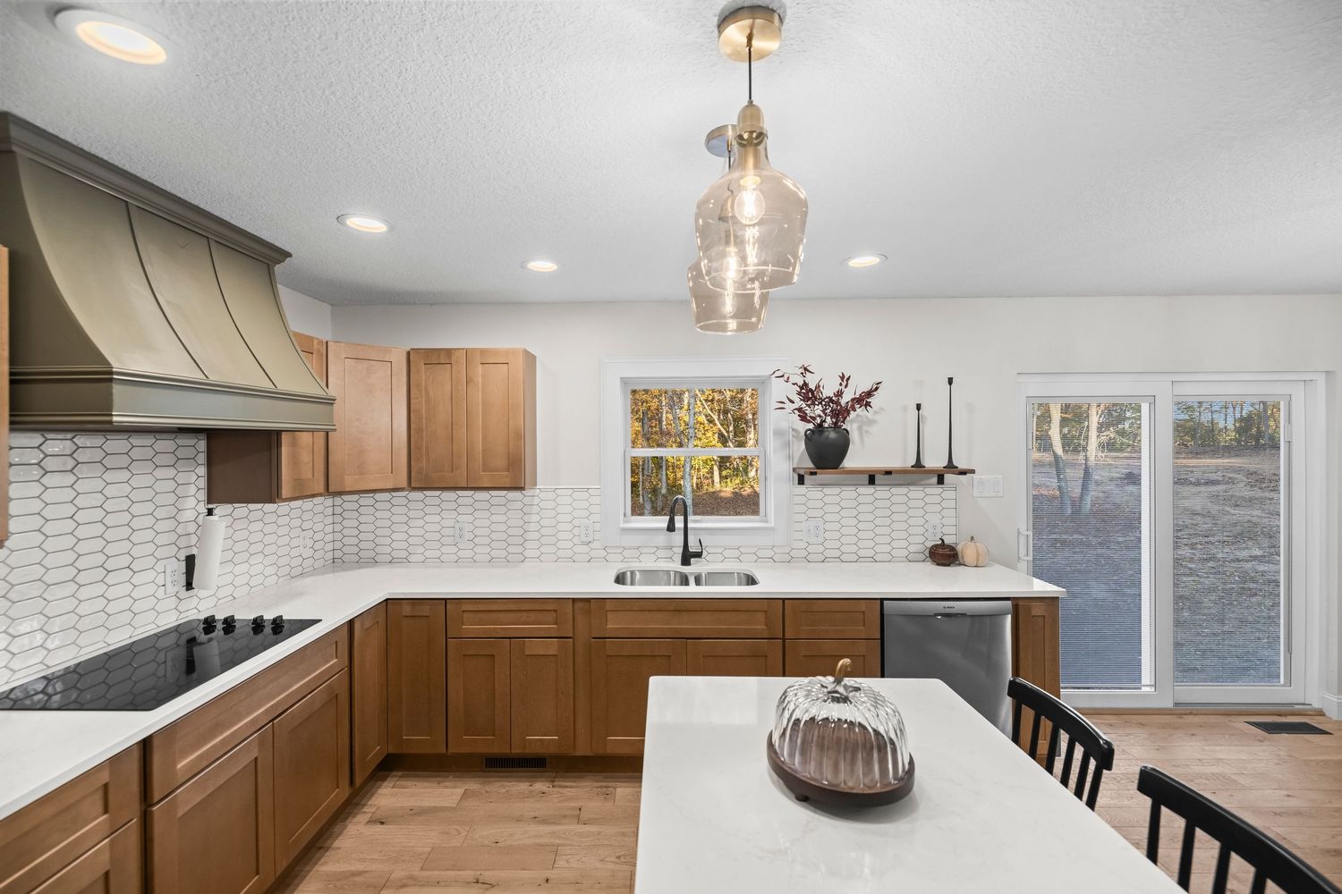 Modern kitchen with wood cabinets, white tile backsplash, black cooktop, pendant lights, and large island on hardwood floors.