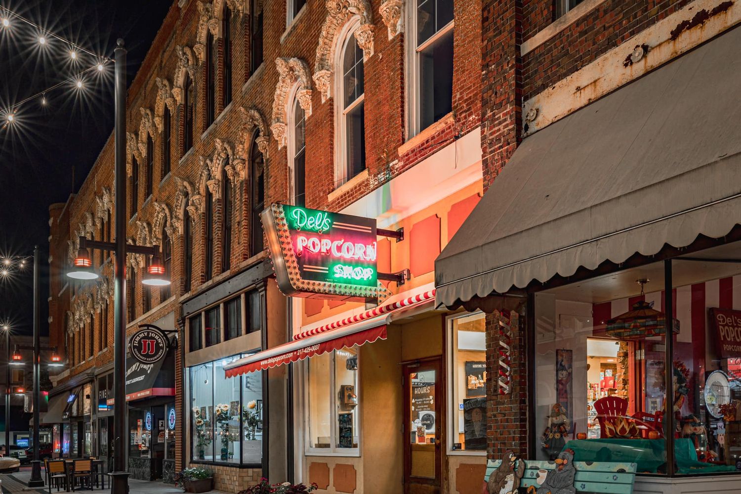 Colorful downtown street at night featuring a retro Dells Popcorn Shop neon sign on historic buildings.