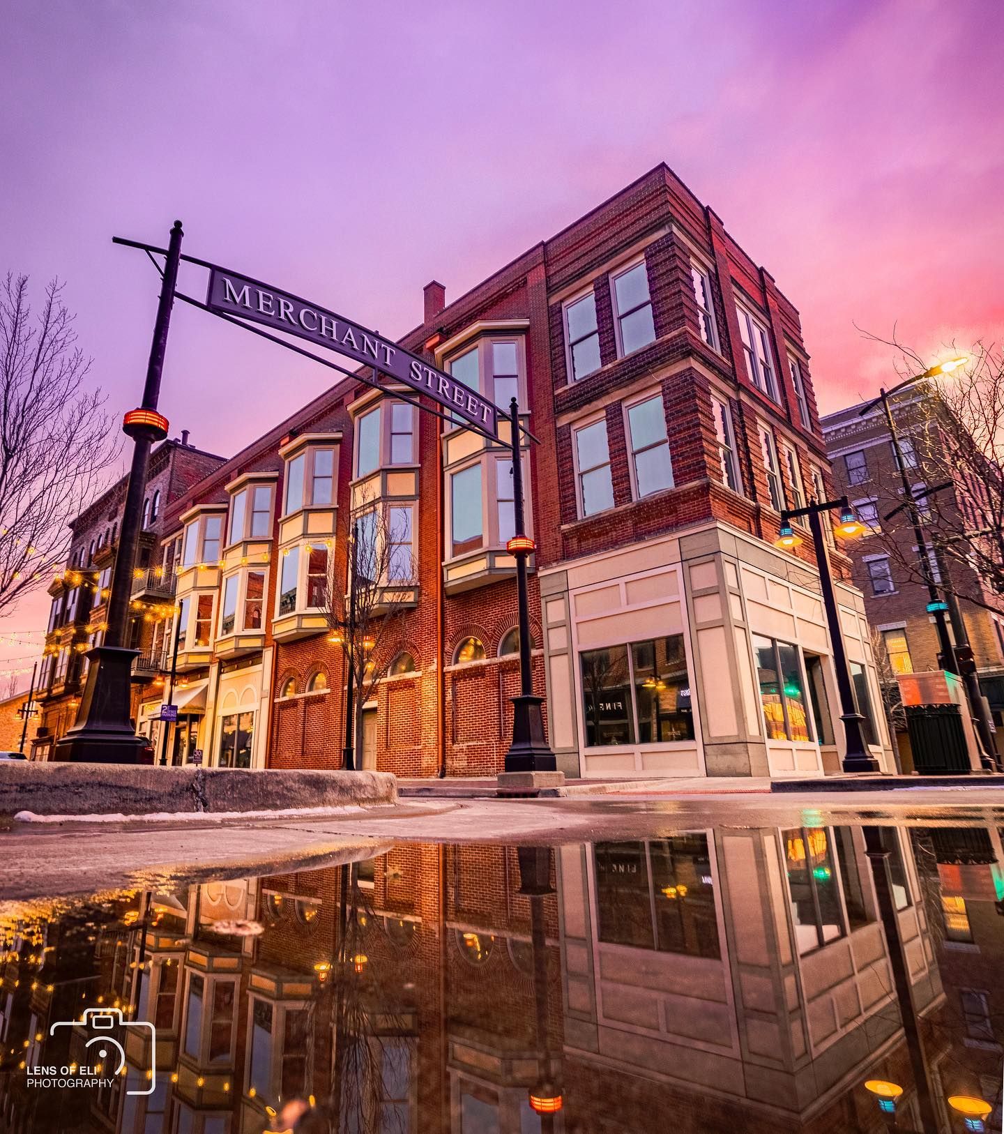 Historic red brick Merchants Street corner building reflecting in a puddle under a vivid purple sunset sky.