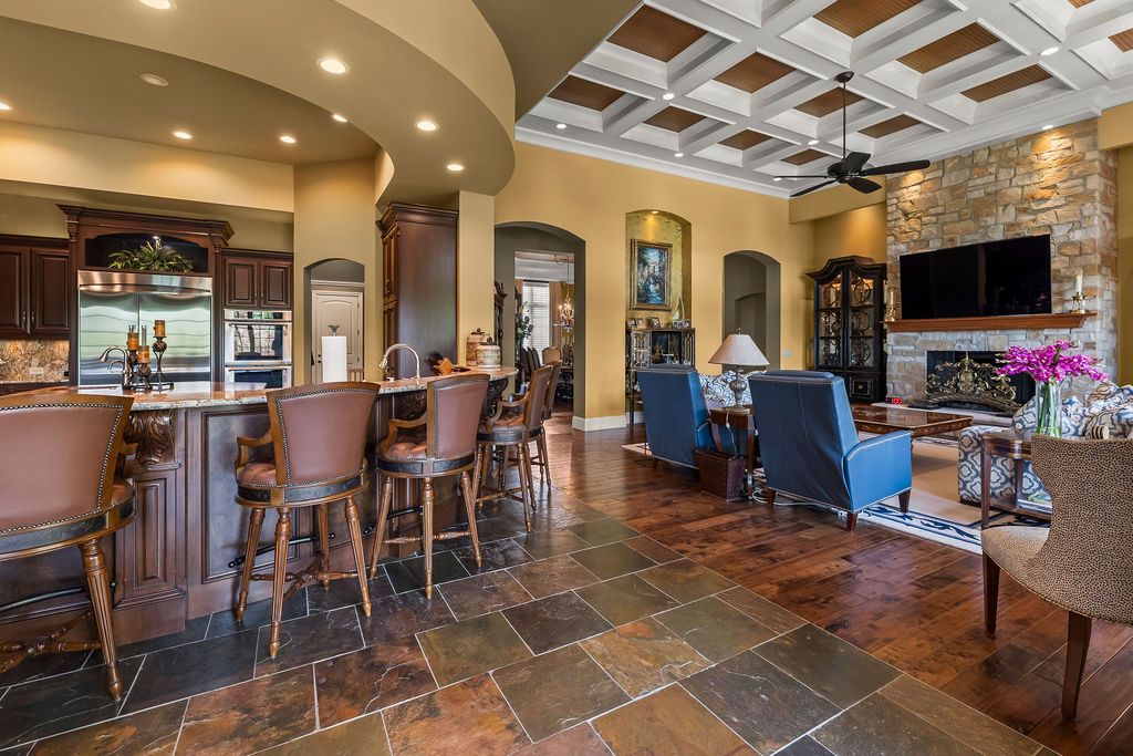 Elegant open-concept living space with coffered ceiling, stone fireplace, bar seating, and slate tile flooring in a luxury home.