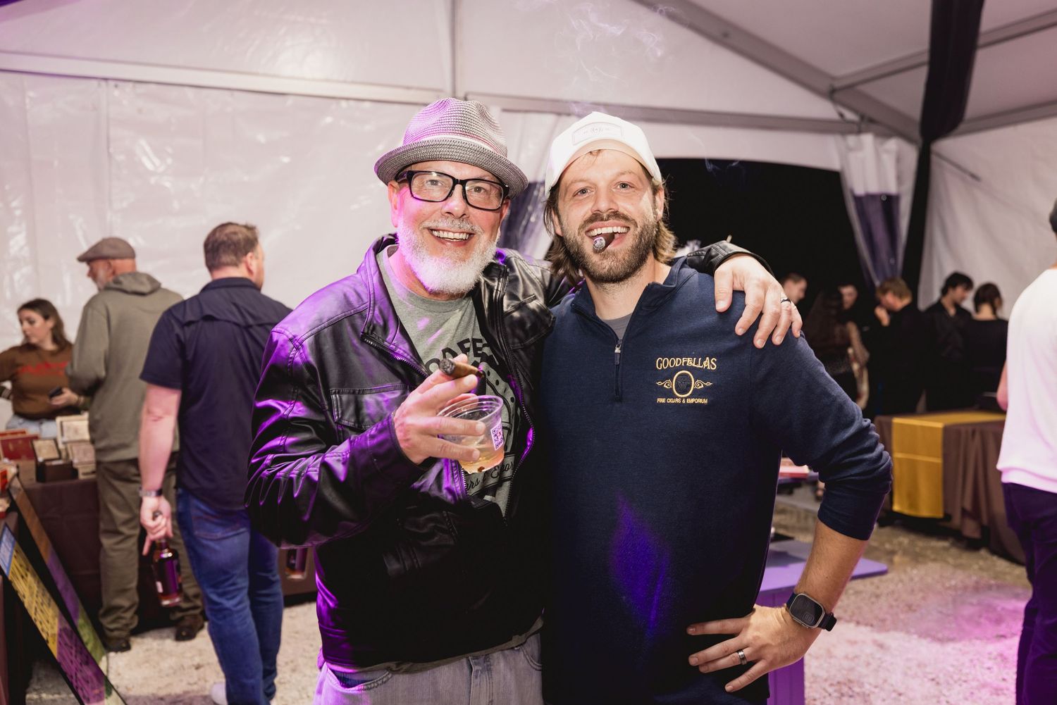 Two men smiling and posing together at a festive indoor event under purple and white lighting.