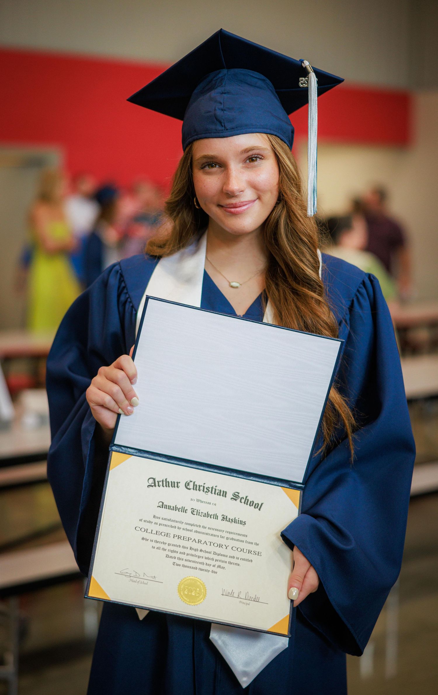Smiling female graduate in blue cap and gown holding diploma from Arthur Christian School.