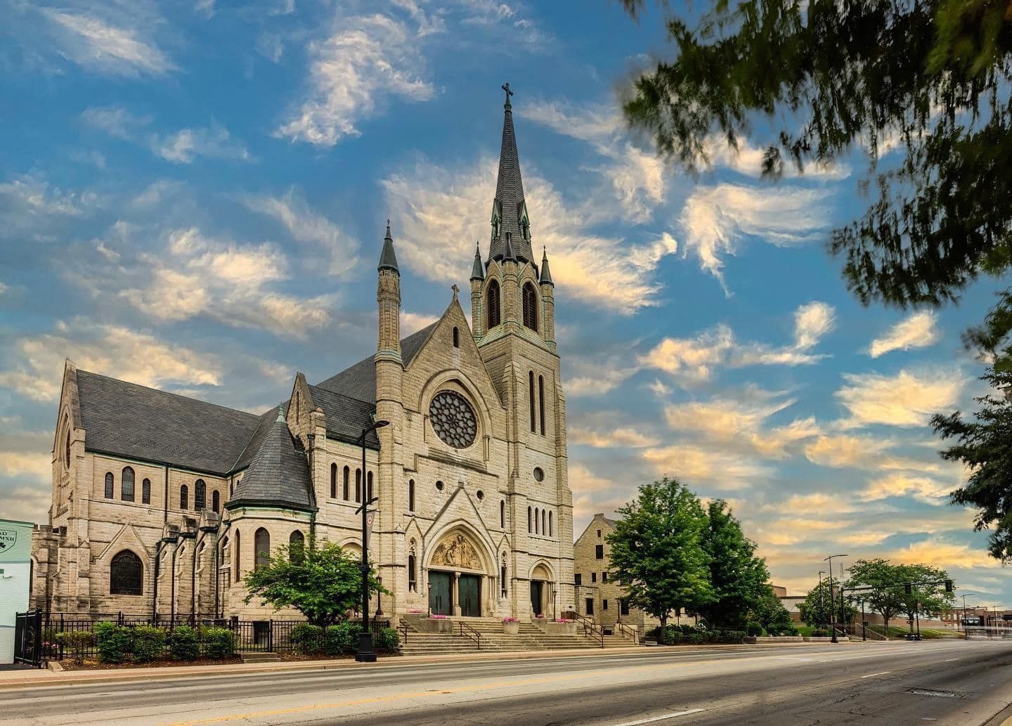Grand Gothic Revival church with tall spire and rose window under dramatic blue sky with golden clouds.