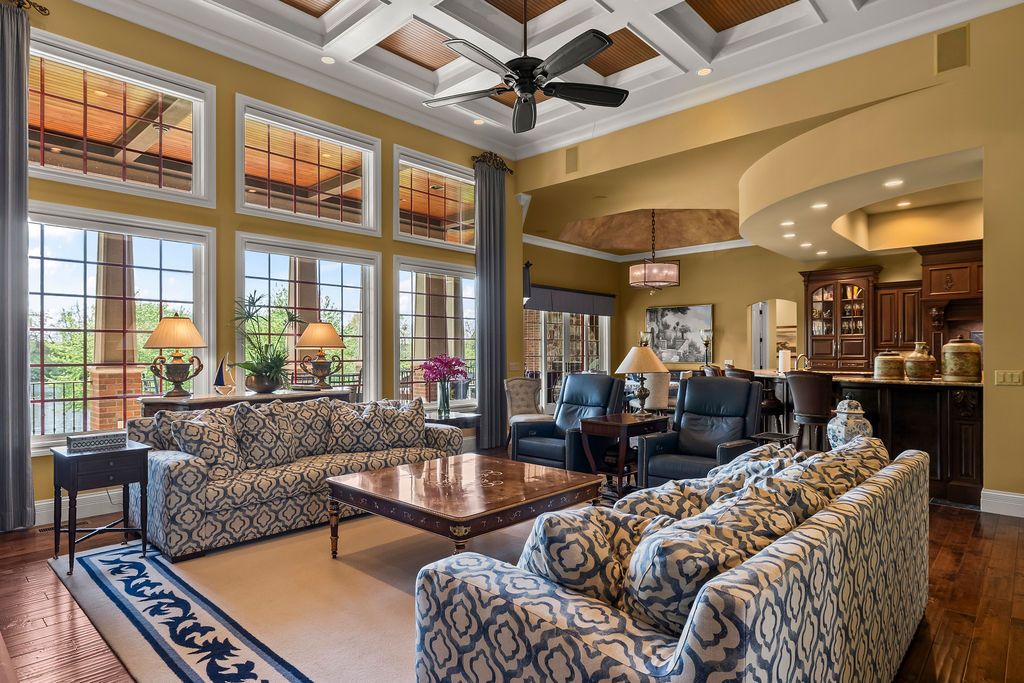 Elegant living room with coffered ceilings, patterned sofas, hardwood floors, and large windows flooding the space with natural light.