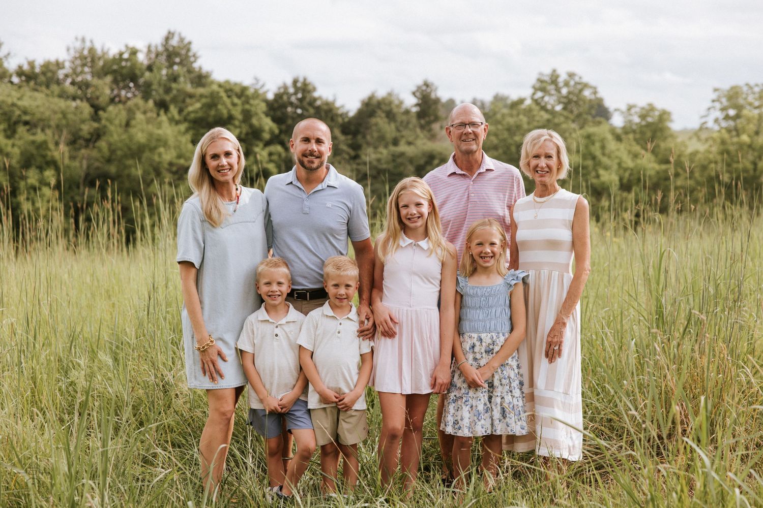 Family of eight posing together in a lush green meadow wearing coordinated casual outfits.