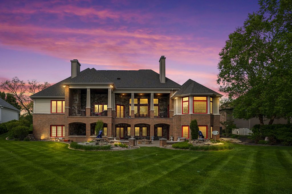 Stunning two-story brick luxury home with illuminated balconies and lush green lawn under a vibrant purple and pink sunset sky.