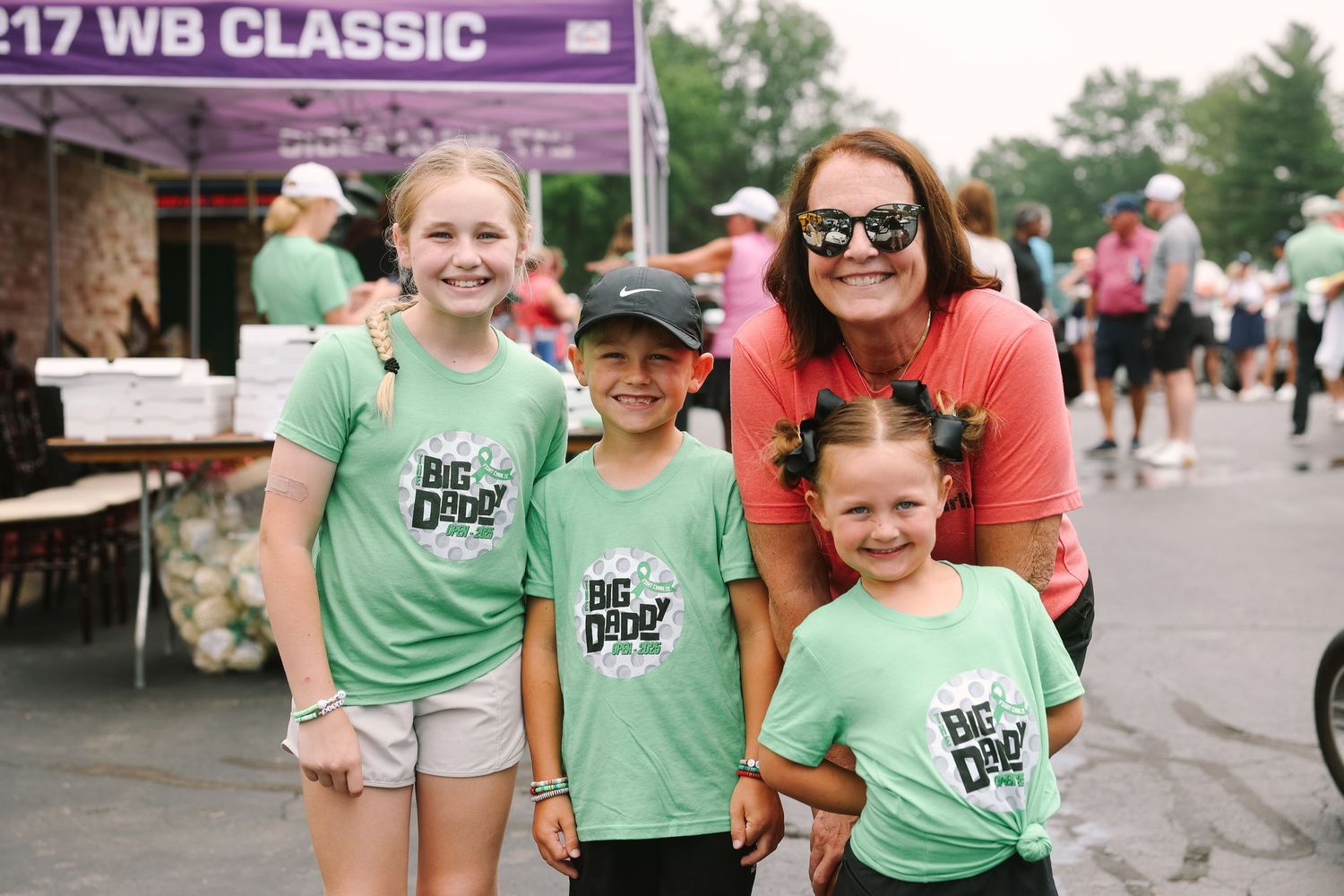 A woman and three children wearing matching green Big Dude shirts pose at the WB Classic event.