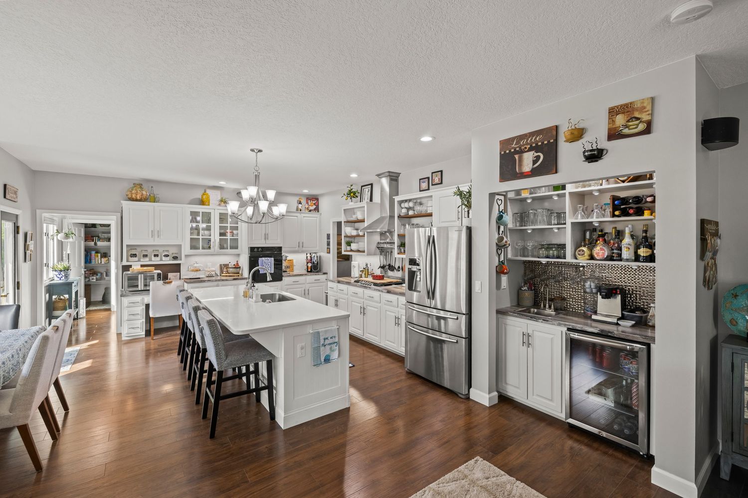Spacious open-concept kitchen with white cabinets, large island with bar seating, stainless steel appliances, and hardwood floors.
