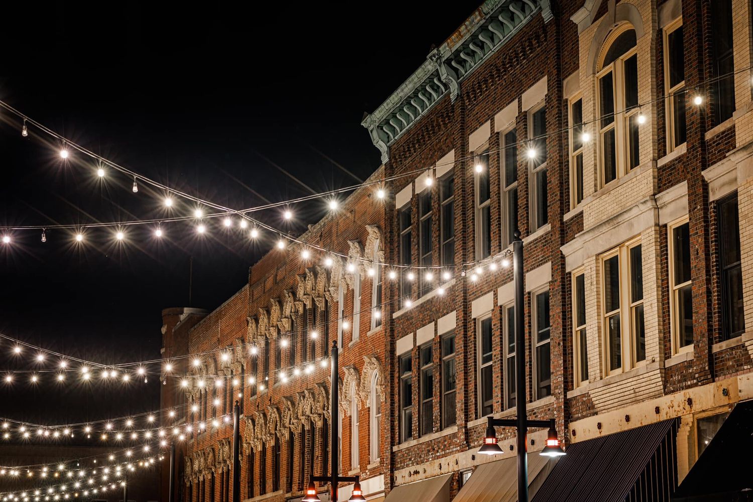 Charming historic brick buildings illuminated by warm string lights on a vibrant downtown street at night.