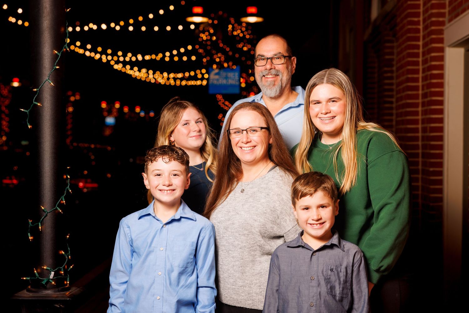 Family of six smiling together under string lights at evening indoor celebration event.