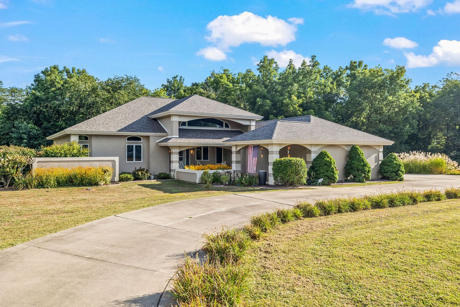 Large ranch-style home with circular driveway, manicured lawn, and mature trees on sunny day.