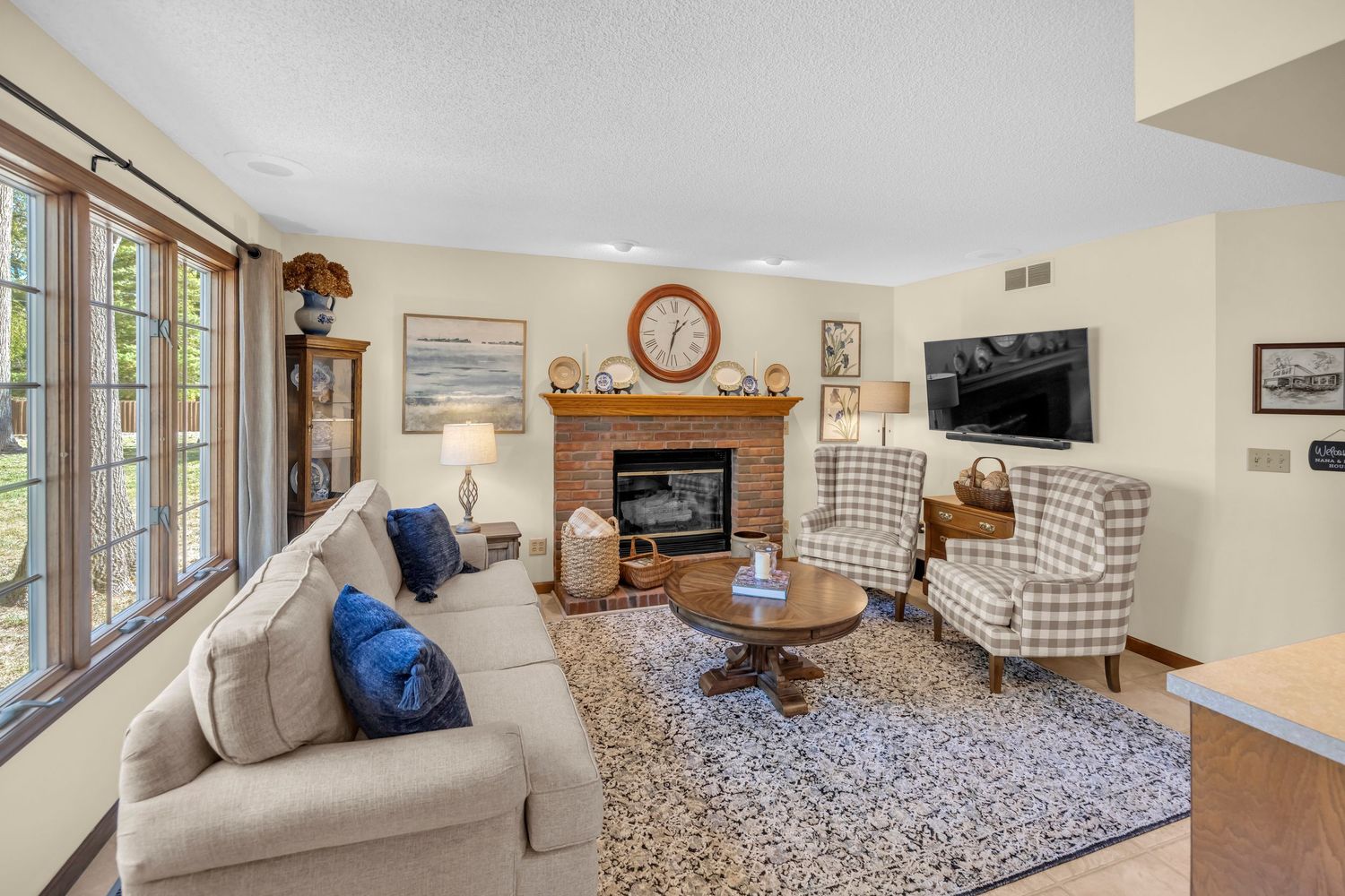 Cozy living room with brick fireplace, plaid armchairs, beige sofa, and blue accent pillows.