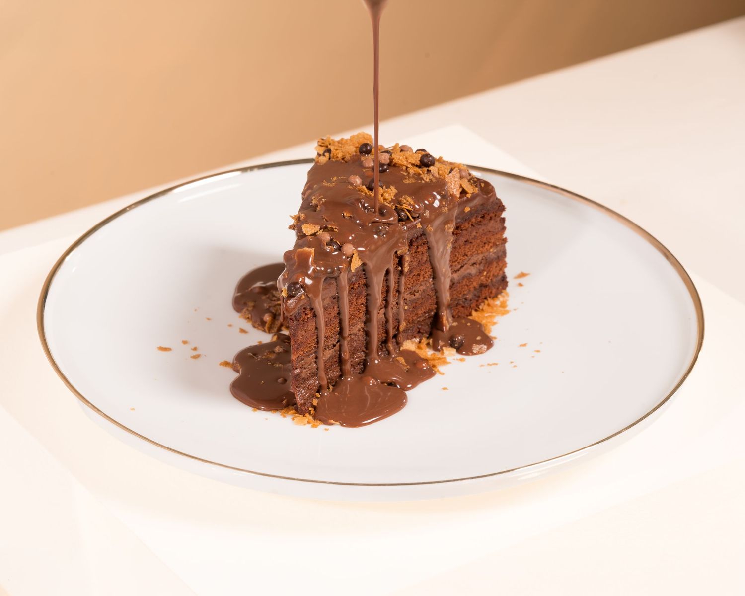 Chocolate cake slice with ganache drizzle and crumble topping on white gold-rimmed plate.