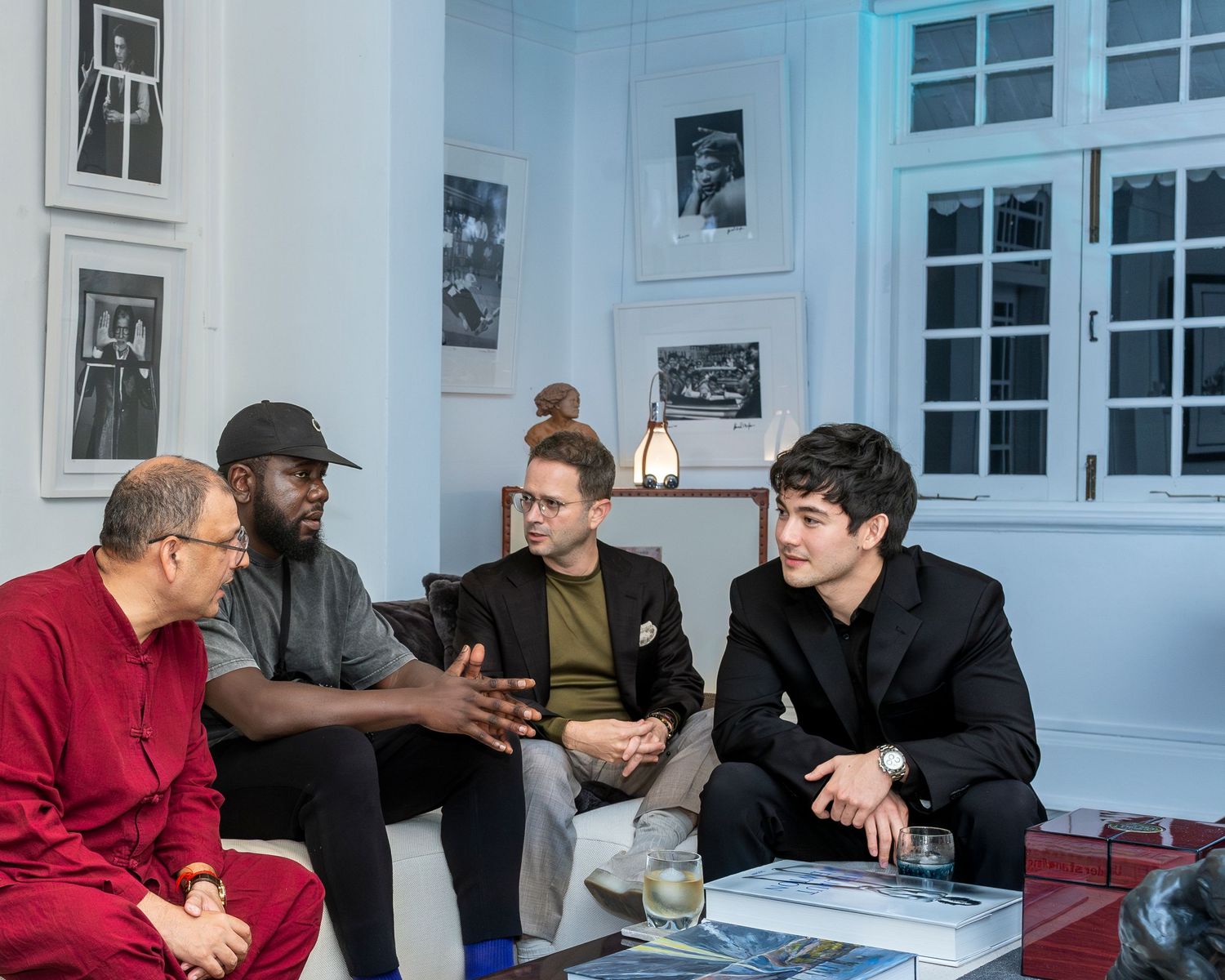 Four men engaged in conversation while seated in a stylish living room with artwork on walls.