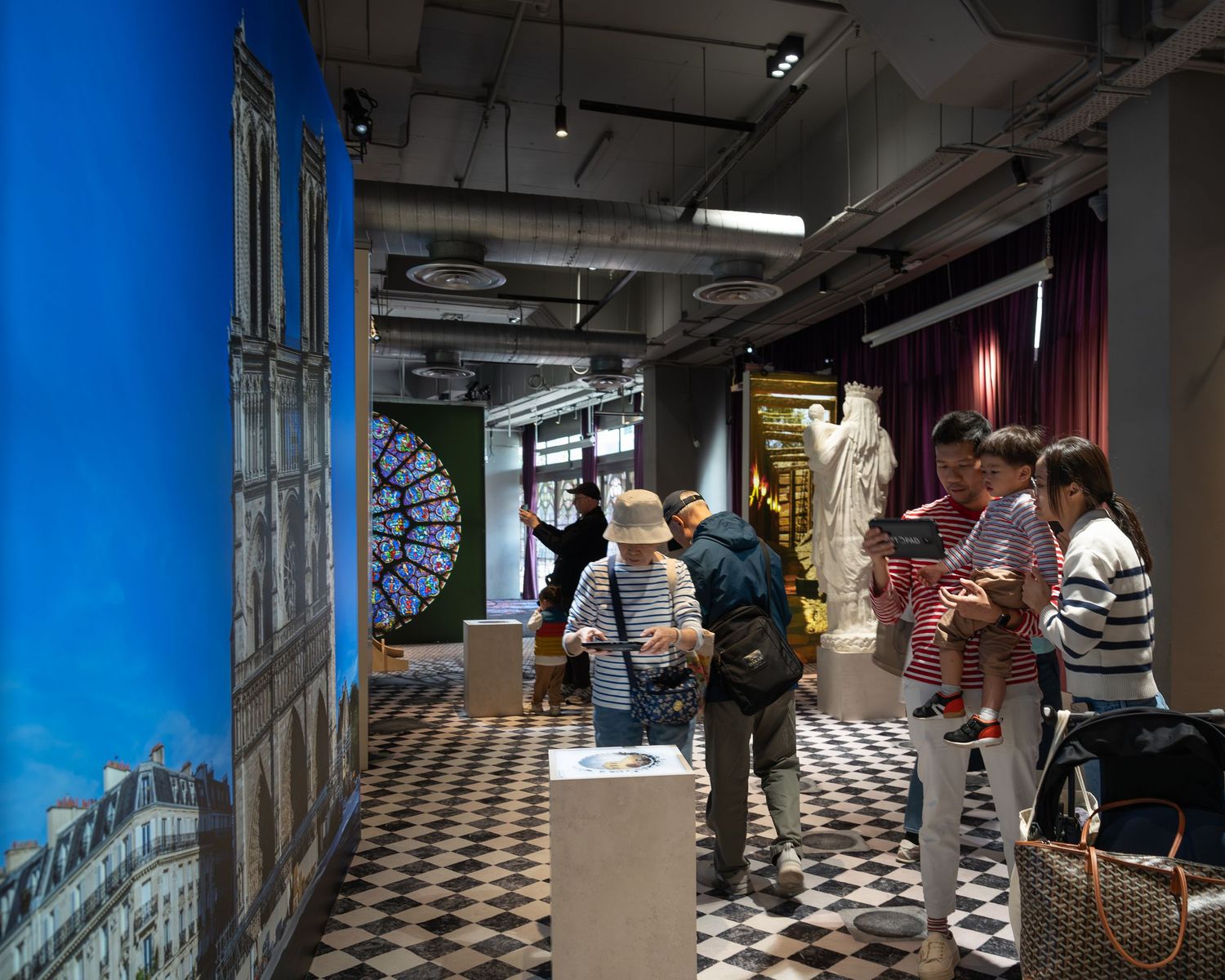 Visitors walking through a museum exhibit featuring large murals of Notre-Dame Cathedral in Paris.