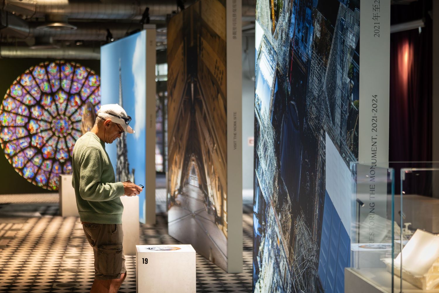 A man examines colorful cathedral artwork displays in a modern museum exhibition hall.