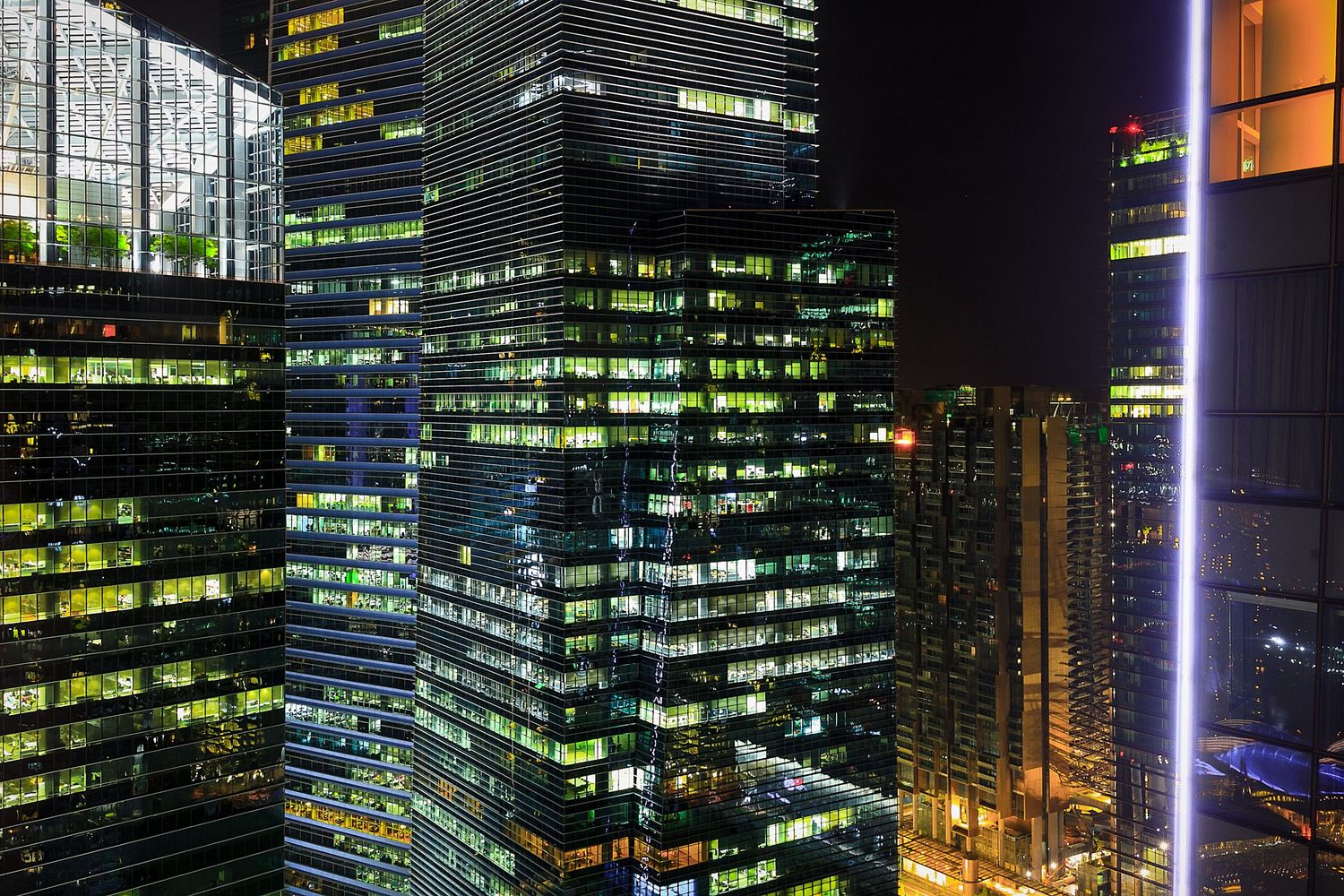 Illuminated skyscrapers at night with glowing office windows in modern city.