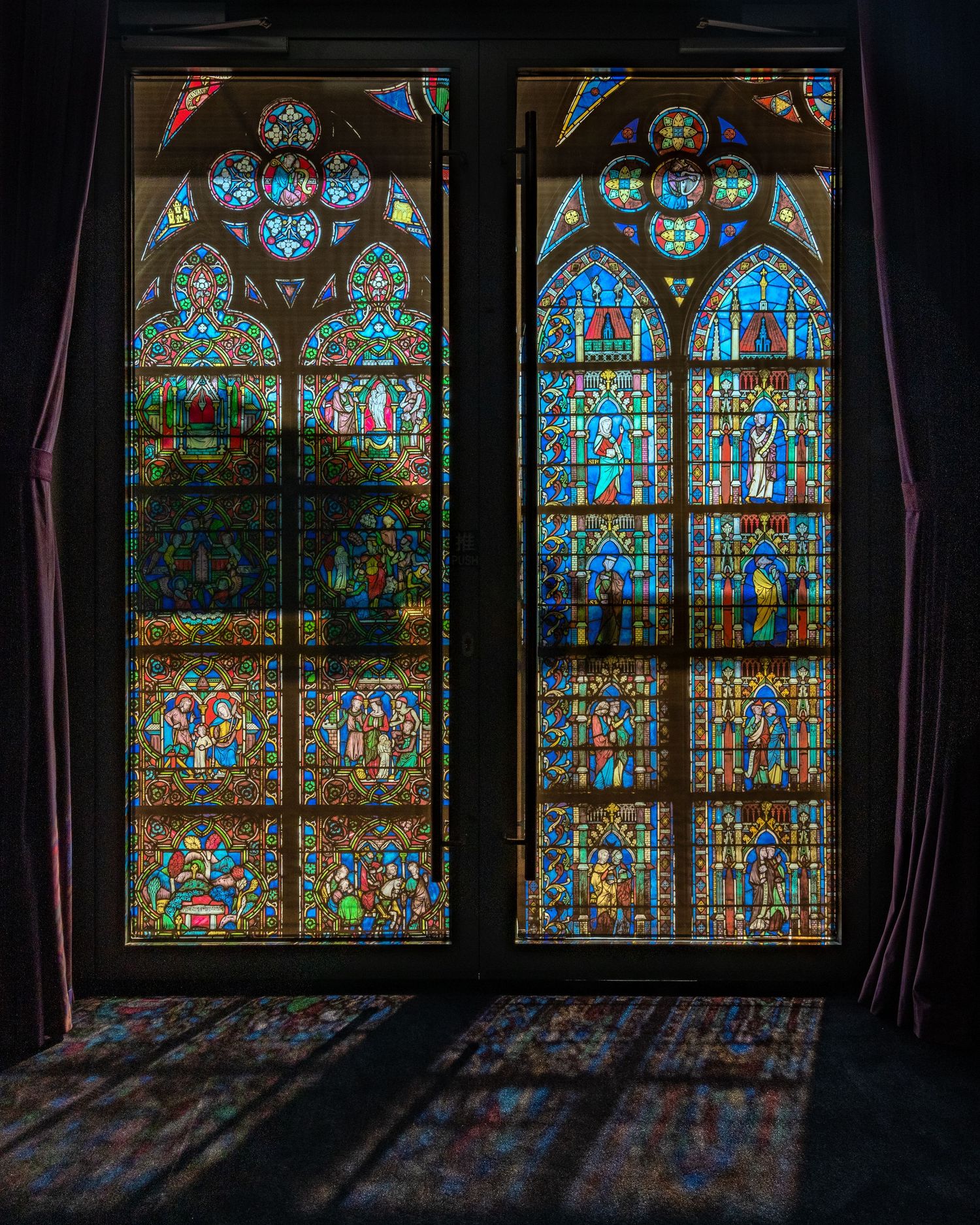 Stunning Gothic cathedral stained glass windows casting colorful light patterns on dark floor.
