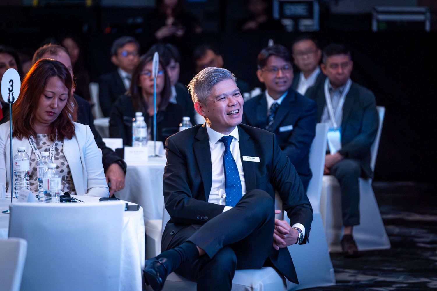 Man in suit smiling while seated at a professional conference event.