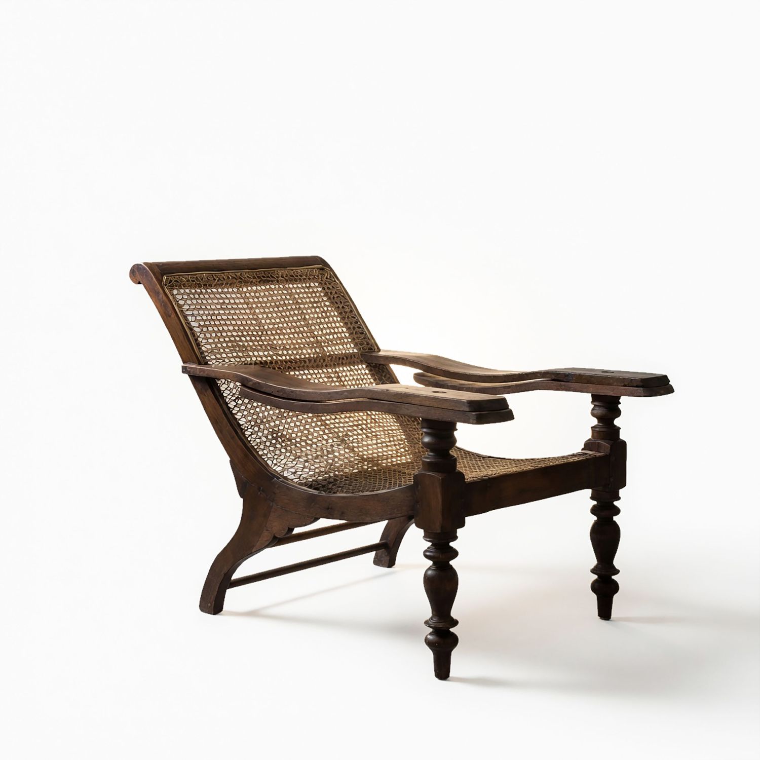 Antique wooden plantation chair with cane back and seat, carved turned legs, and extended armrests.