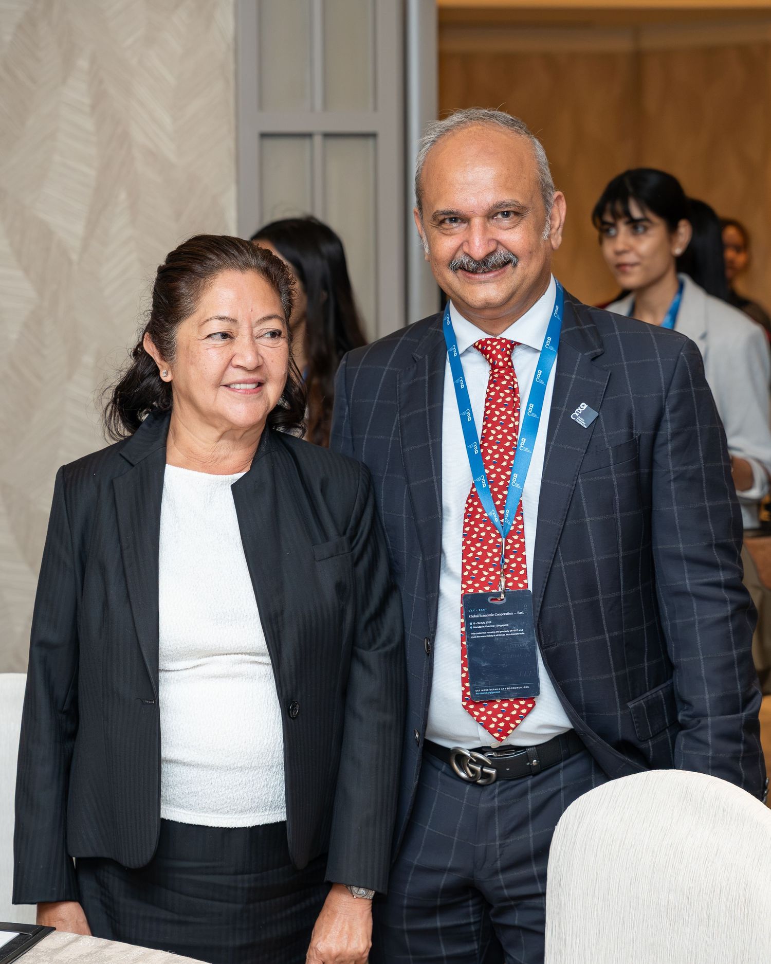 Two professionals in formal attire smile together at a corporate conference event.